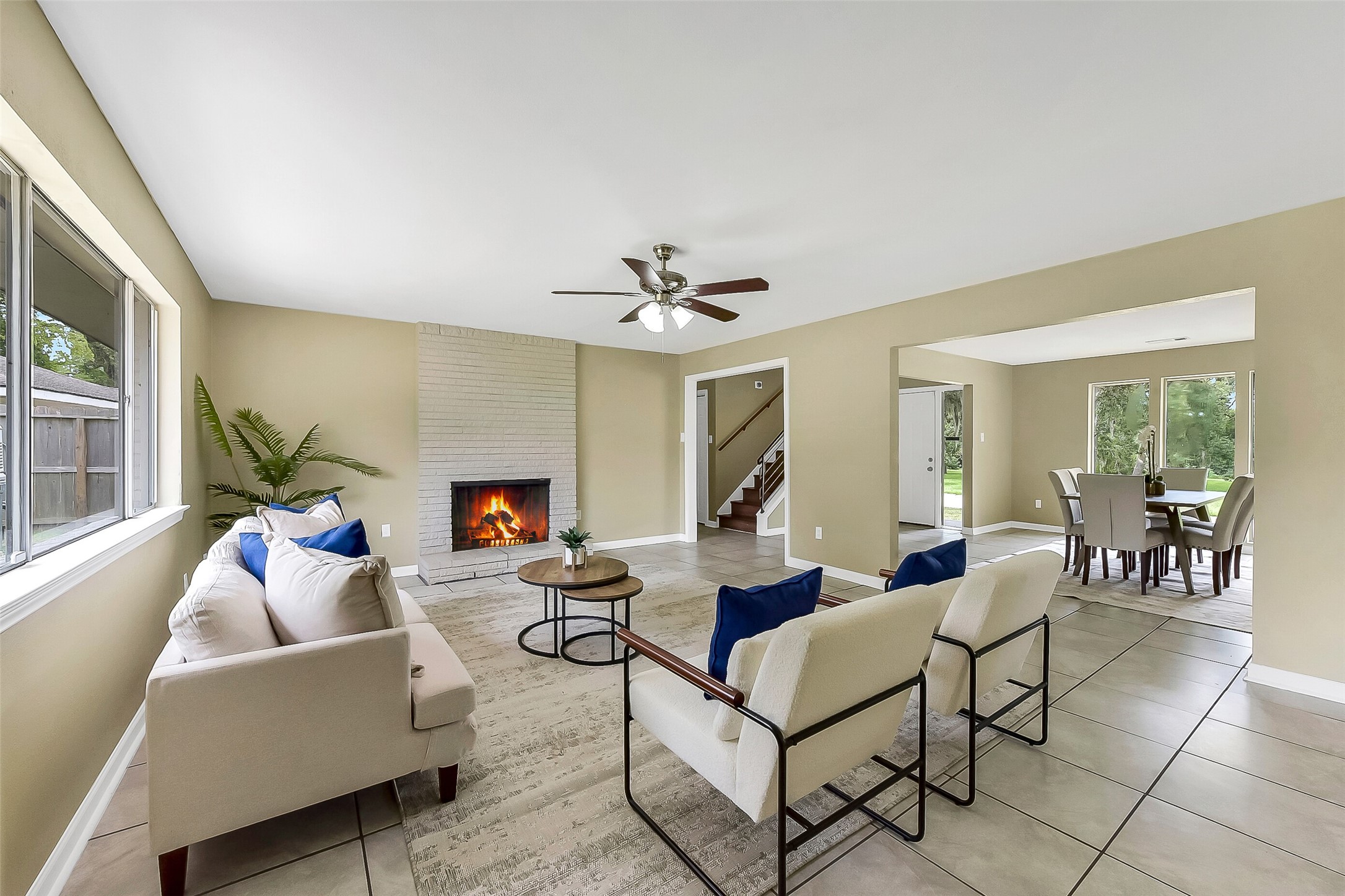 Continue into this spacious family room with a cozy brick fireplace, large windows for natural light, neutral tones, and easy-care tile flooring that flows into the dining area.