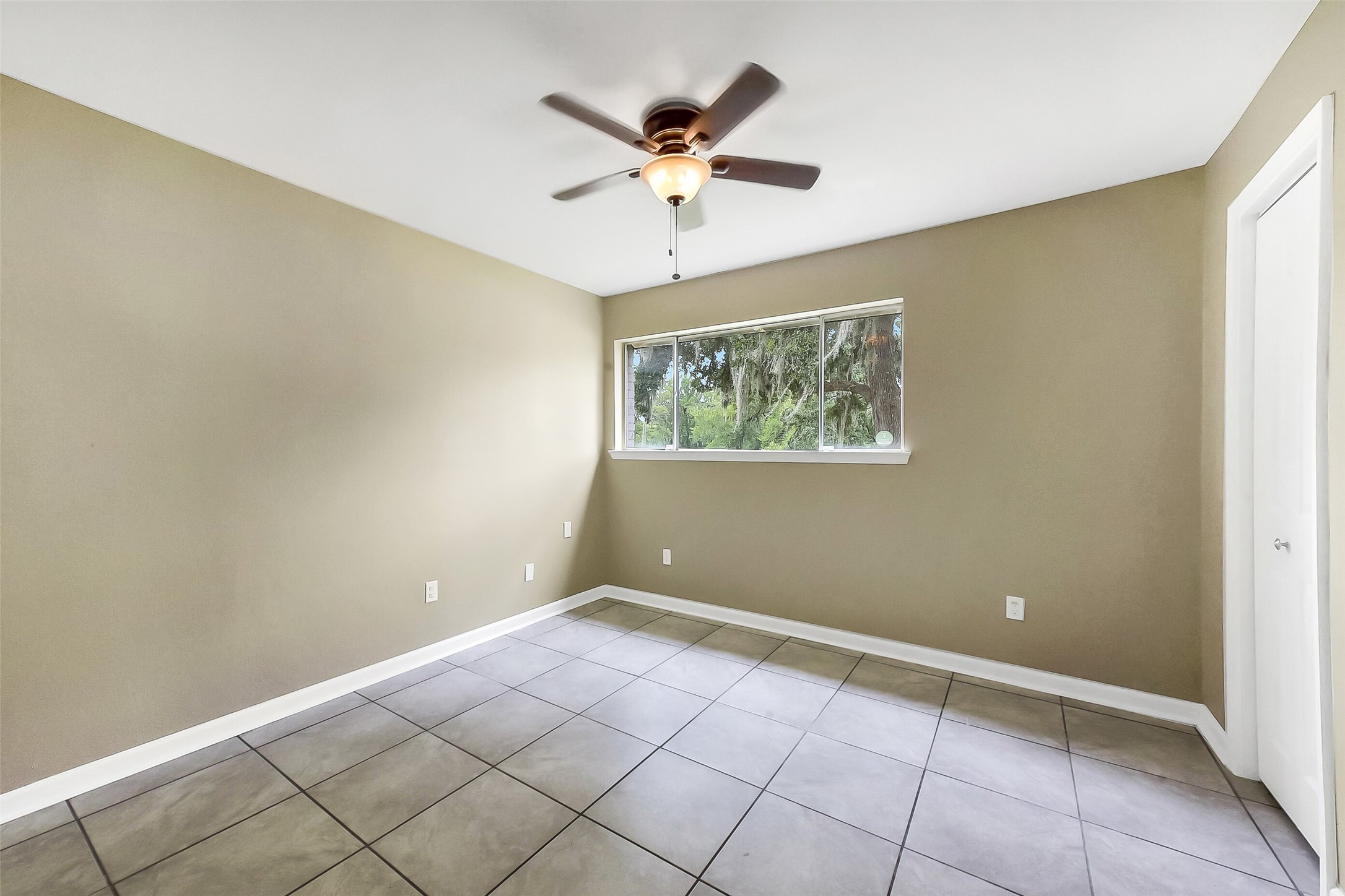 First-floor guest bedroom featuring neutral paint, tile flooring, a ceiling fan, and a large window that fills the space with natural light.