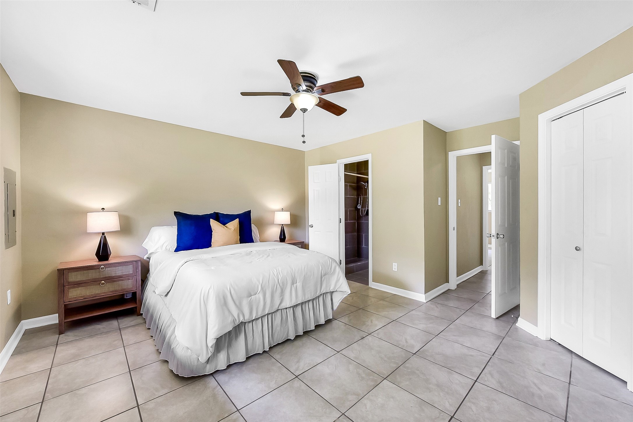 This first-floor primary suite offers a peaceful retreat with neutral tones, tile flooring, a ceiling fan, and a large window that fills the room with natural light. An en-suite bath provides added privacy and convenience.
