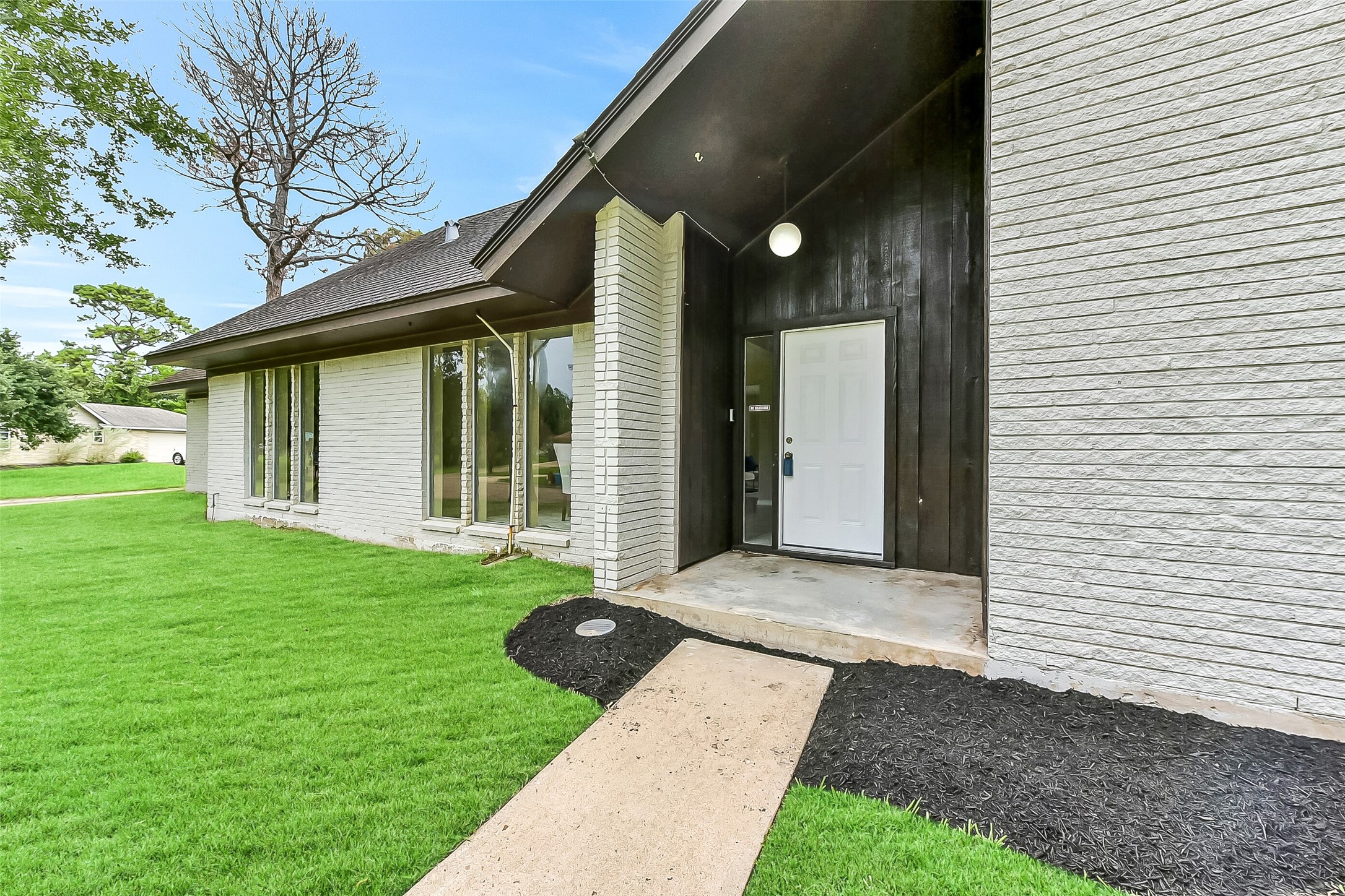A welcoming covered front entry framed by tall windows sets the tone for this 3,019-square-foot home, showcasing fresh exterior updates and a modern contrast of painted brick and dark wood accents.