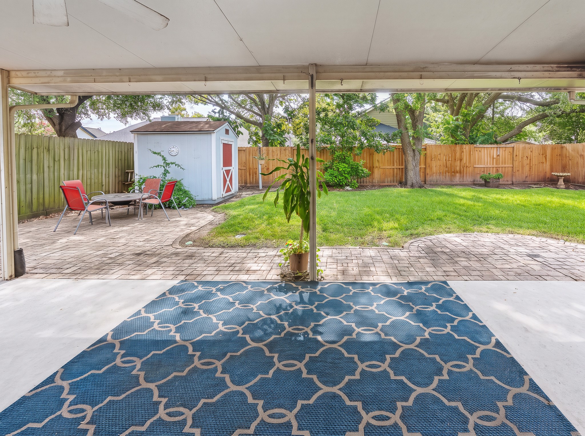 A covered patio provides easy access to the lush backyard, where a paved seating area, outdoor storage shed, and fire pit create a versatile setting for outdoor relaxation.