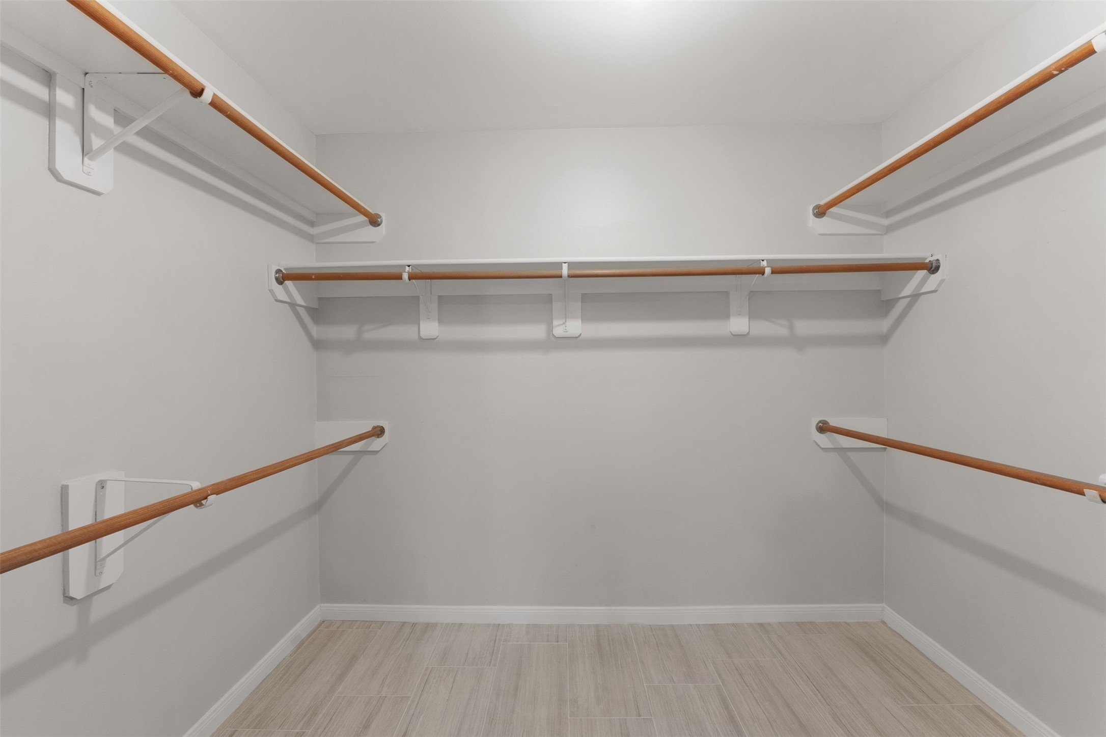 Multi-level wooden hanging rods and built-in shelving maximize organization in this spacious walk-in closet. Soft light-toned wood flooring completes the functional storage space.