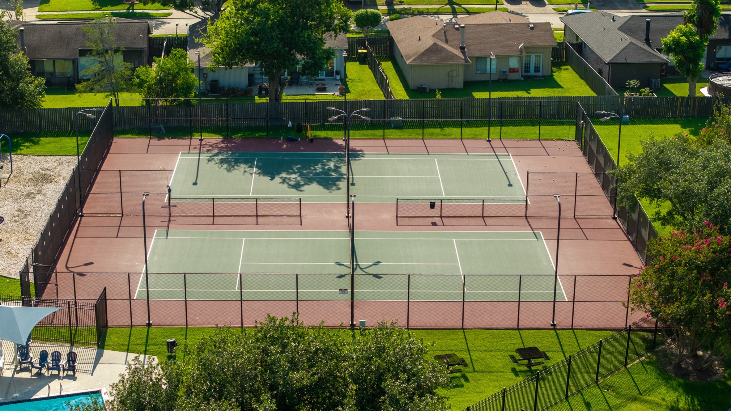 Surrounded by manicured green spaces and tall fencing, this community sports court features two full-sized tennis courts equipped with overhead lighting. Residents enjoy premier recreation options steps away, alongside access to a nearby community pool.