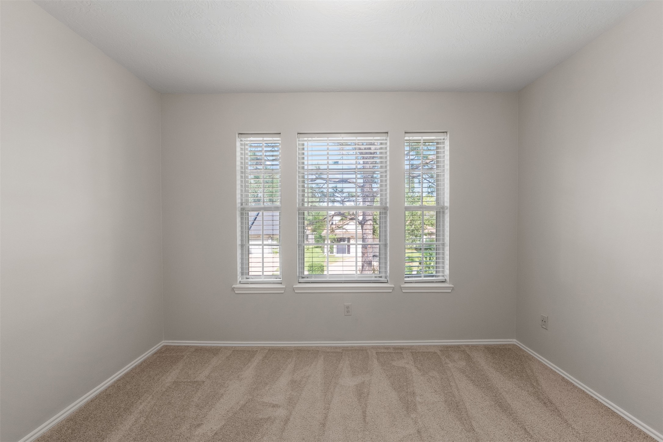 Soft carpet flooring and freshly painted walls frame a triple window that bathes this secondary bedroom in light.