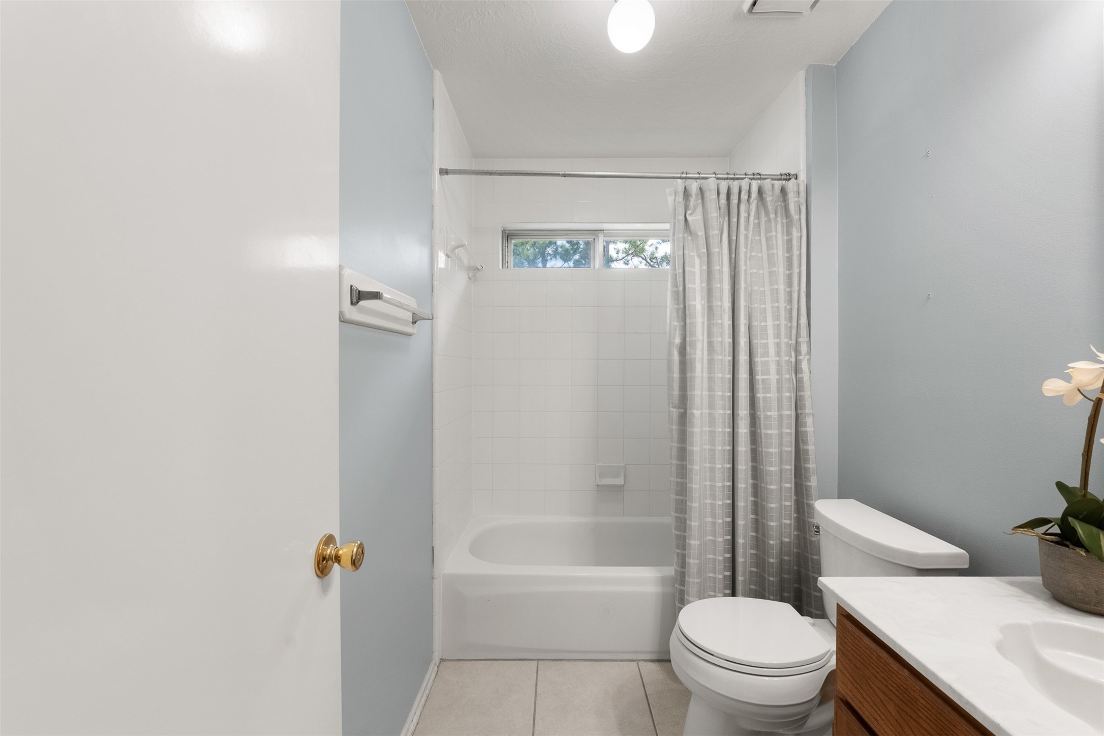 A light blue accent wall and crisp tile flooring bring a fresh look to this secondary bath. Renovated features include a classic tub-and-shower combo, modern vanity, and a transom window that lets in gentle light.