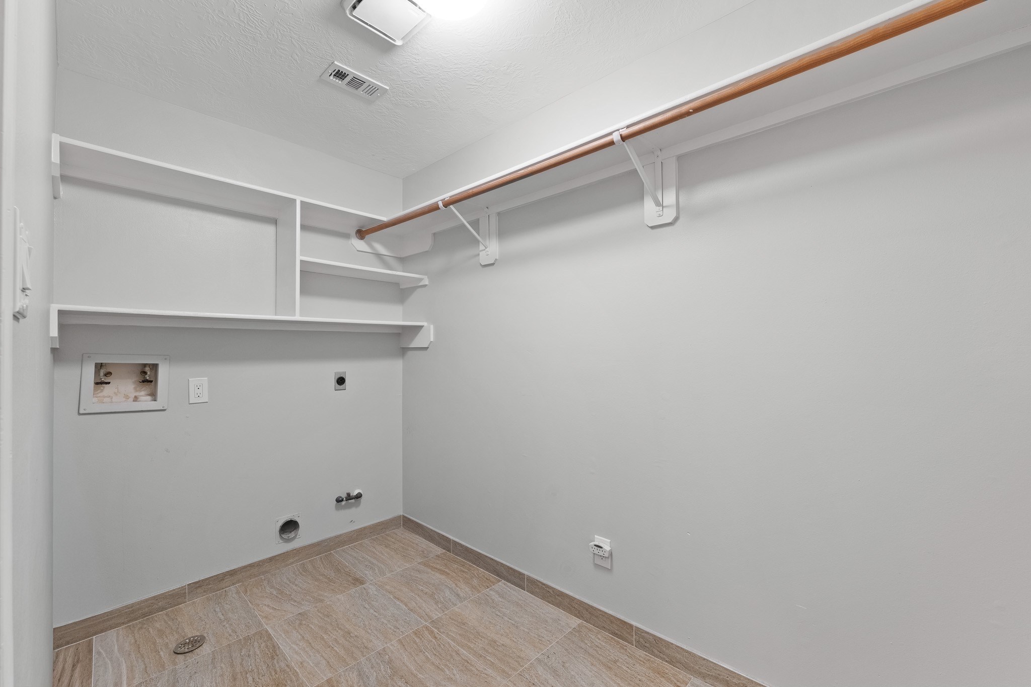 Tile flooring and built-in shelving enhance this functional laundry room, offering overhead clothes rods and hookups.