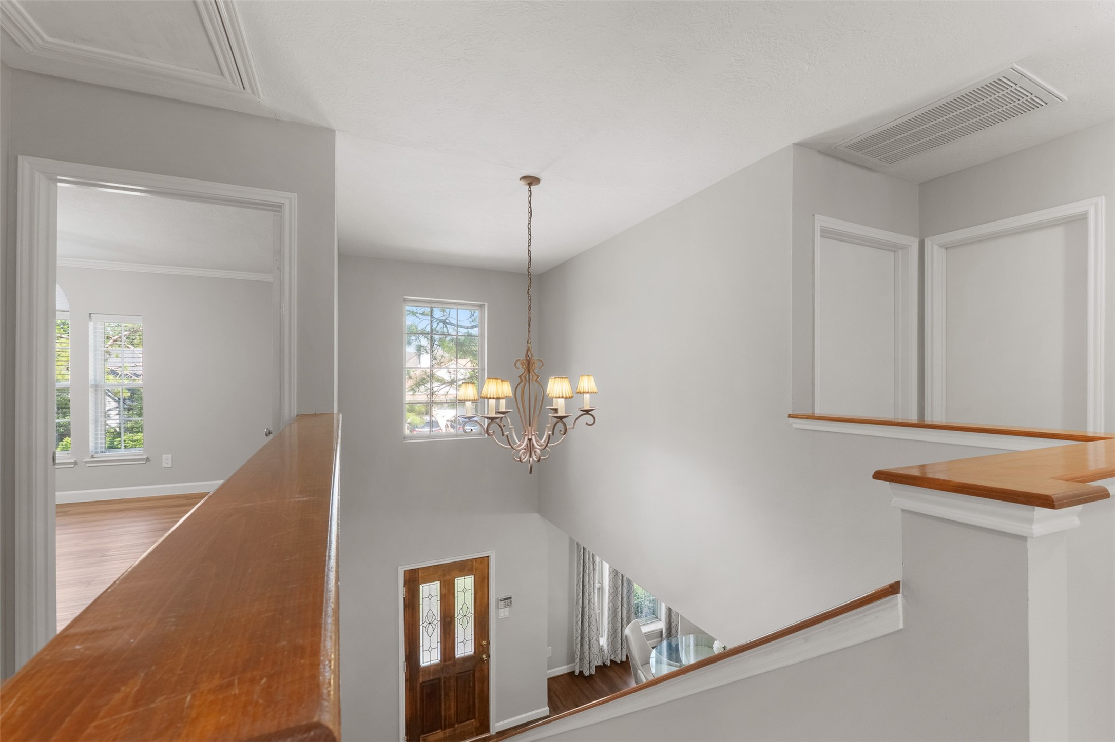 A classic chandelier suspends over the multi-story entry, illuminating the open second-floor hallway and stairwell. Neutral wall paint and wood-topped railings unite the upper landing with views of the lower level below.