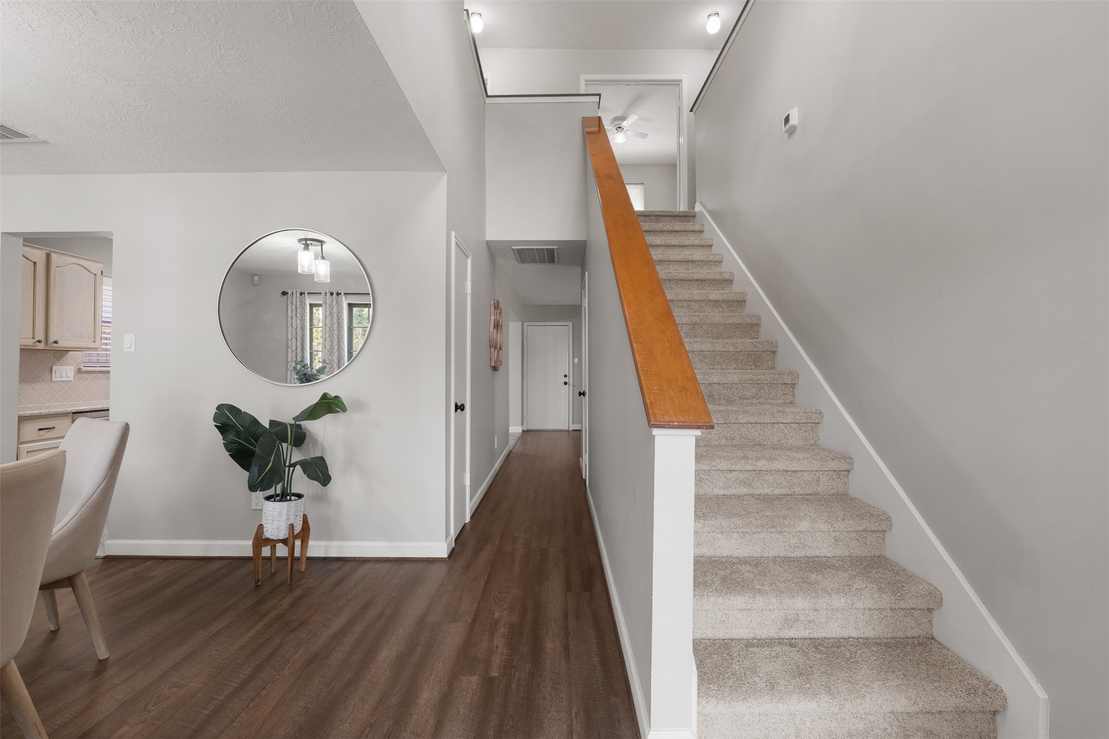 Featuring plush carpeted stairs with a warm wood handrail, this soaring entry connects the lower living areas to the upper level. Rich wood-look flooring stretches past a sunlit dining nook down a central hallway, offering an open and cohesive flow.