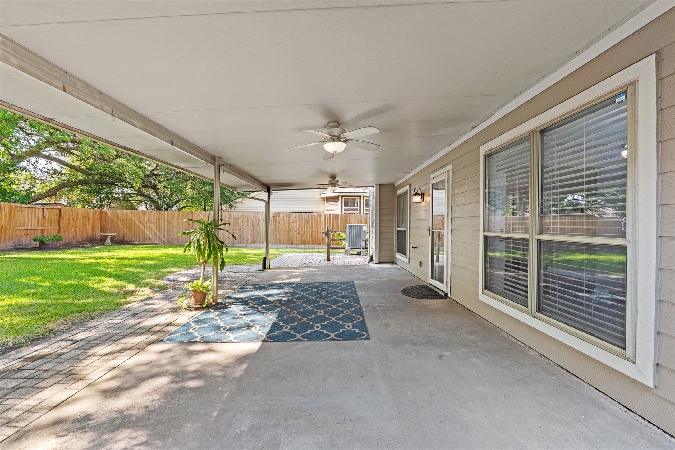 Extending from the home's rear exterior, a deep covered patio equipped with dual ceiling fans overlooks the expansive backyard lawn and paver patio. Large windows and a glass-paneled back door provide easy access and uninterrupted sightlines to the interior living spaces.