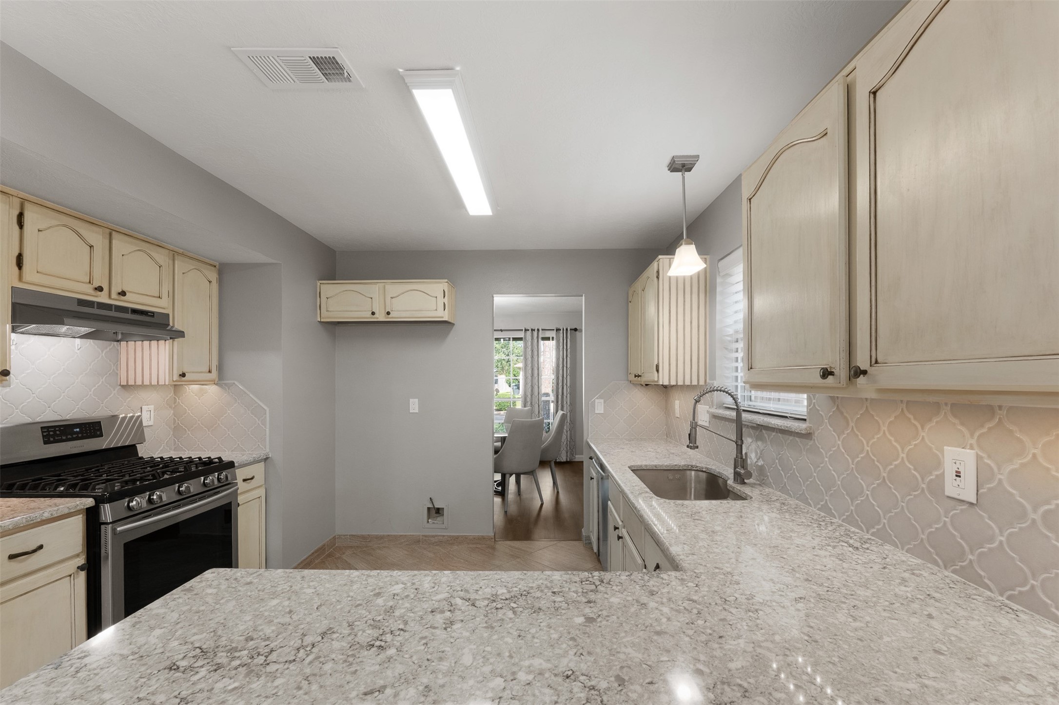 Equipped with a gas range and spacious dual sink, this kitchen showcases quartz countertops and a designer backsplash. Cream cabinetry provides ample storage, while the expansive counter extends into a functional breakfast bar.