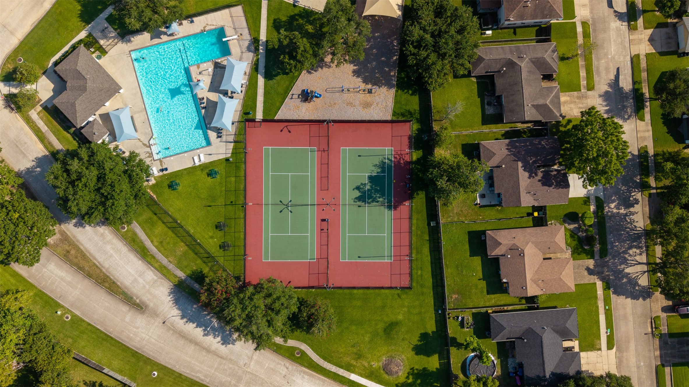 High-angle aerial perspective reveals the neighborhood amenity center, featuring a shimmering community pool and tennis courts.