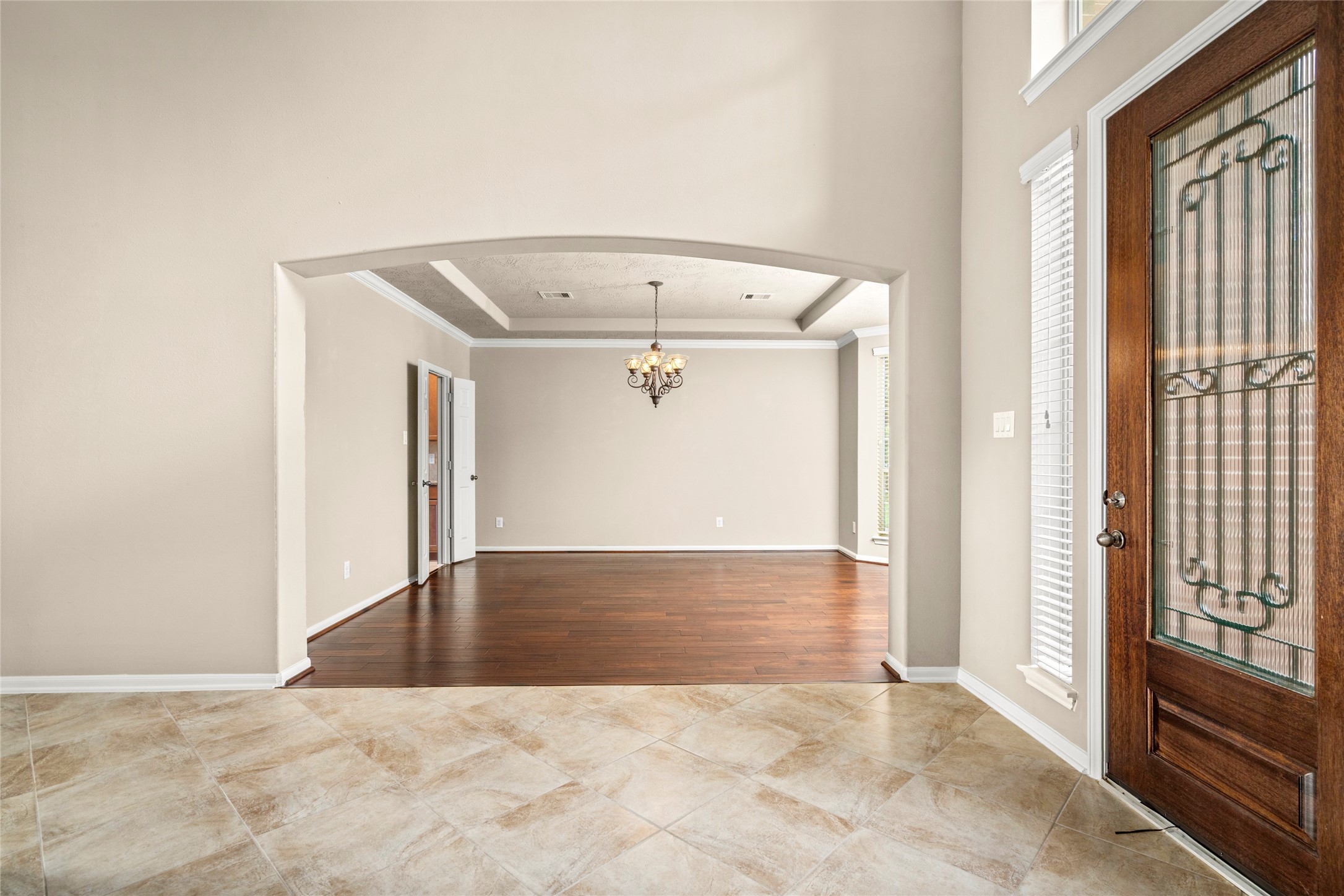 Rich wood flooring, a statement chandelier, and an elegant glass-paneled front door set the tone here, opening gracefully into the formal dining room, designed for unforgettable entertaining.