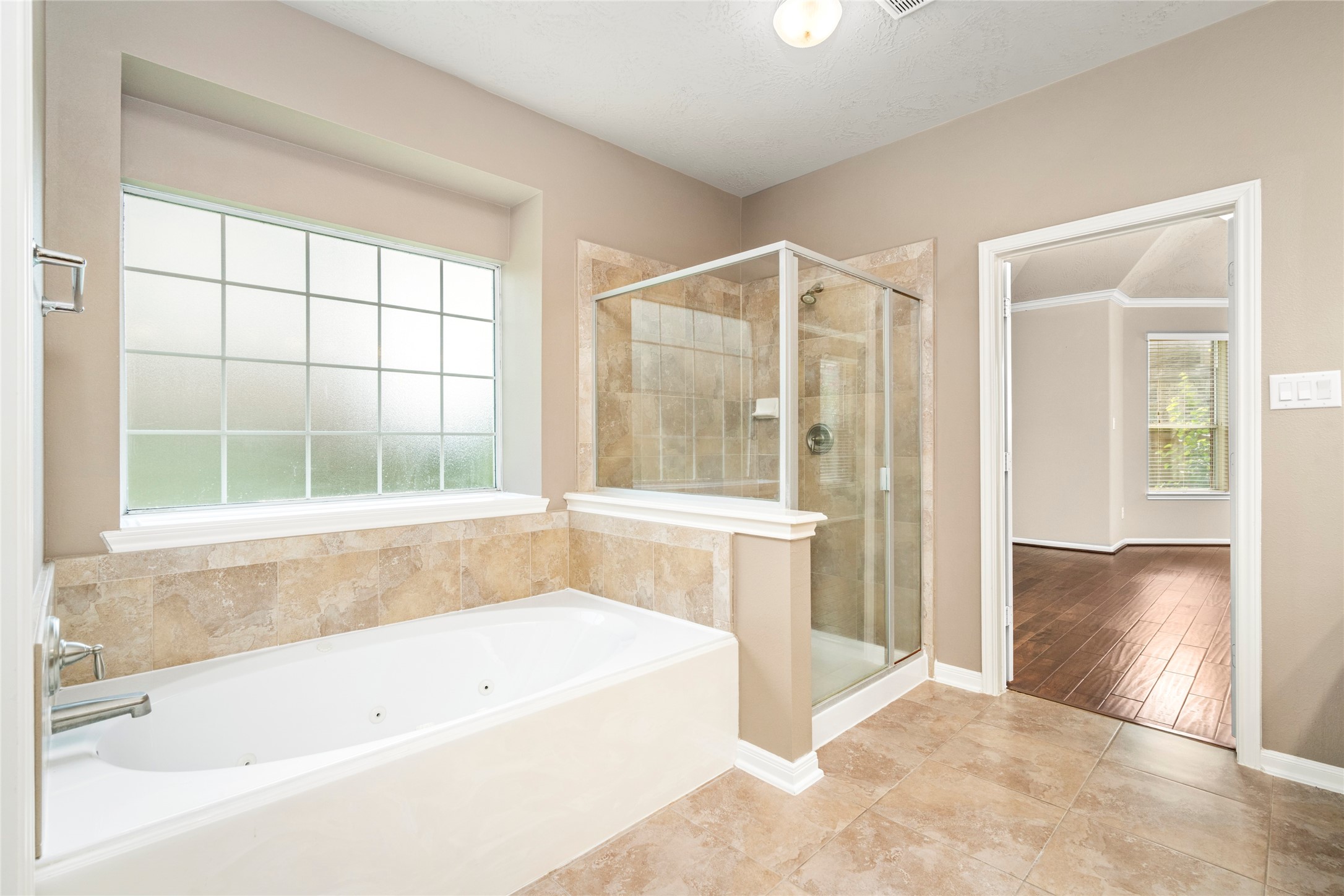 An oversized standalone jetted soaking tub and glass-enclosed shower anchor this spa-caliber primary bath, with elegant tile flooring and a frosted window inviting natural light while preserving privacy.