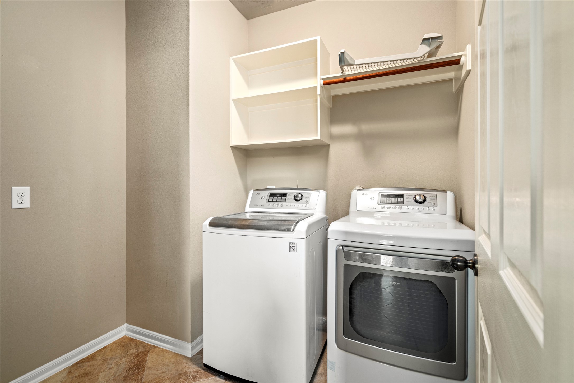 A beautifully appointed laundry suite featuring a stainless washer and dryer that remain with the home, plus custom open shelving for effortless organization.