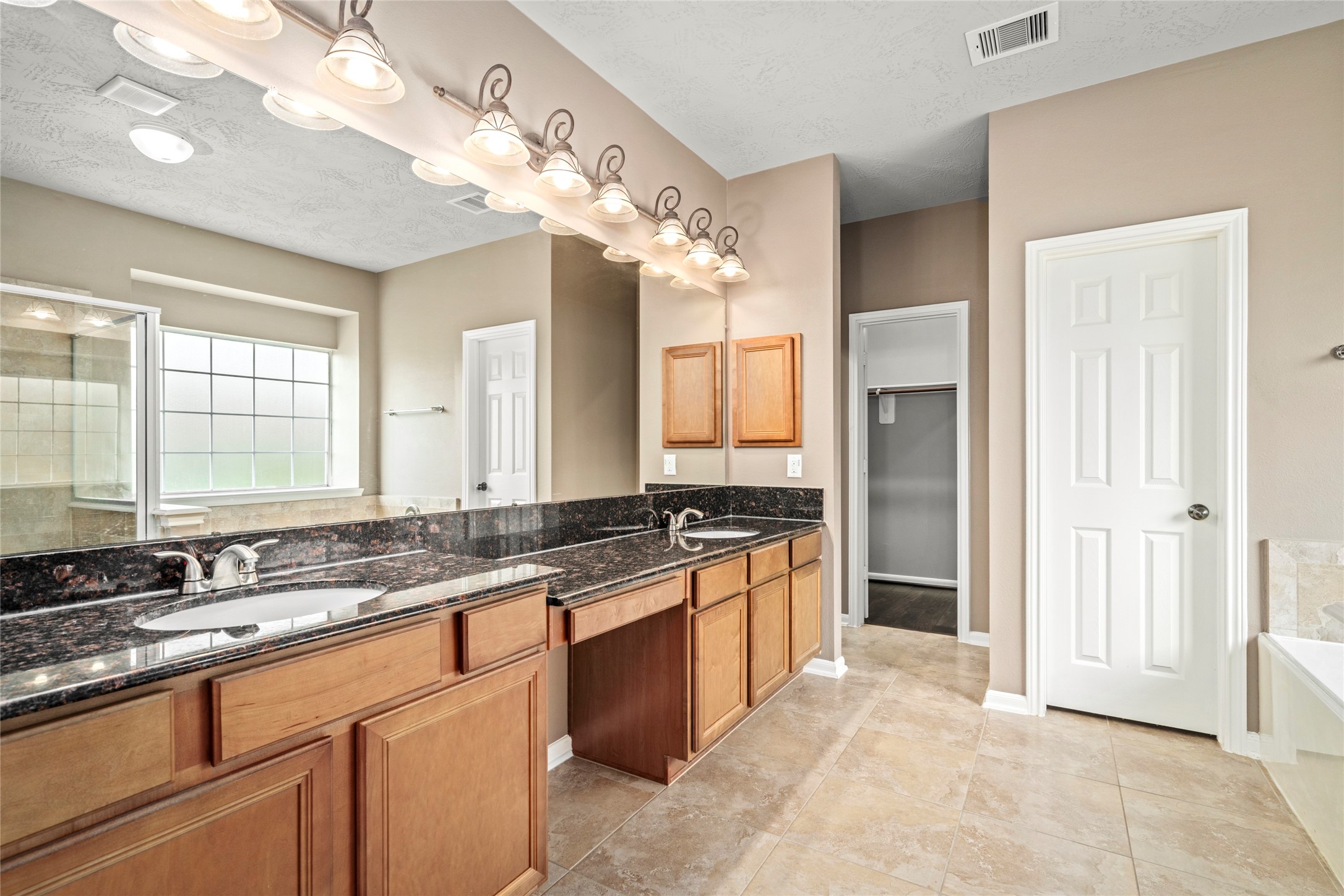 Indulge in a double-sink vanity with granite countertops, abundant cabinetry, and designer lighting, a luxurious retreat designed for daily indulgence.