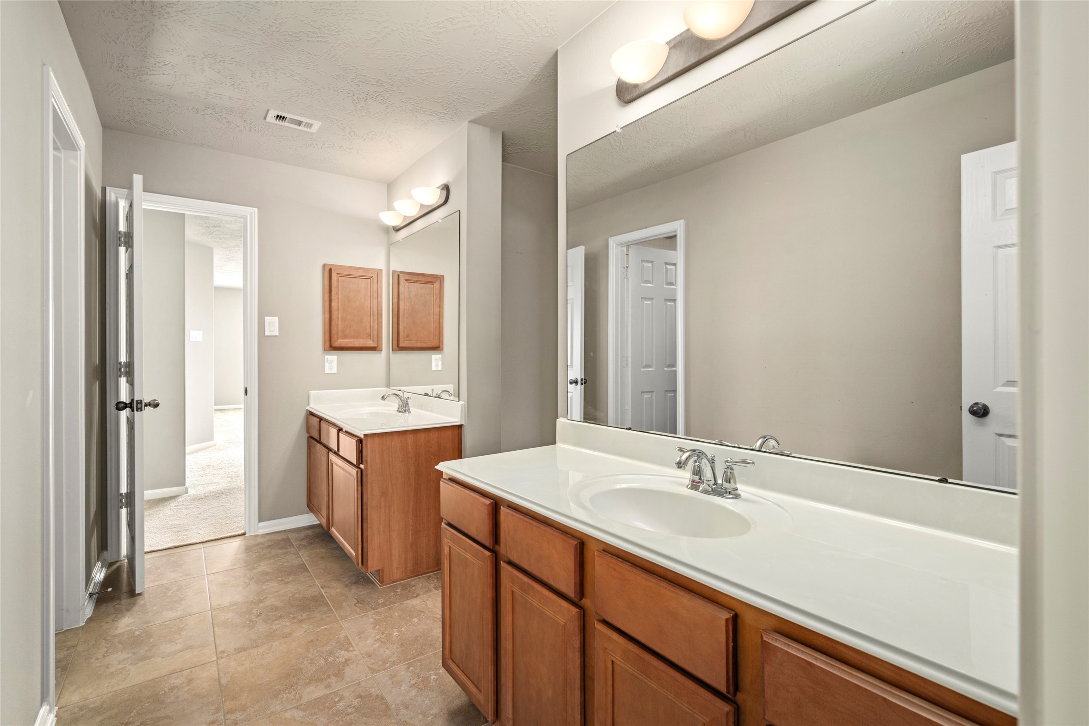 A spacious double-vanity bath with rich wood cabinetry, oversized mirrors, and tile flooring serves the upstairs bedrooms with style and function.