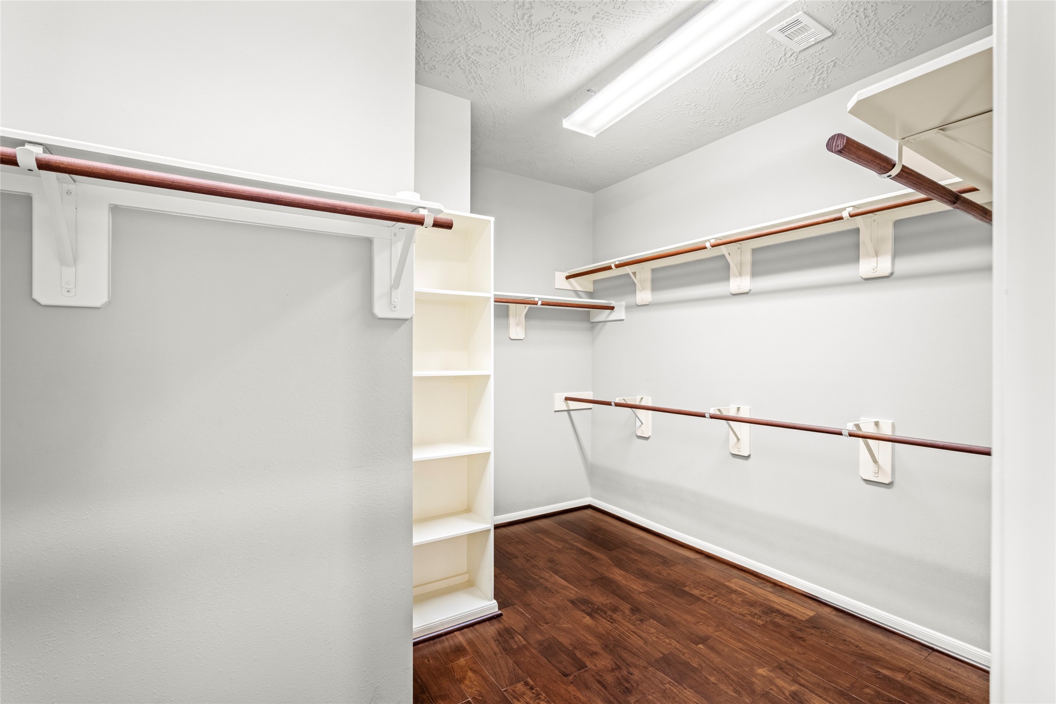 The oversized primary walk-in closet features rich wood flooring and generous hanging storage, closet space designed with the discerning homeowner in mind.
