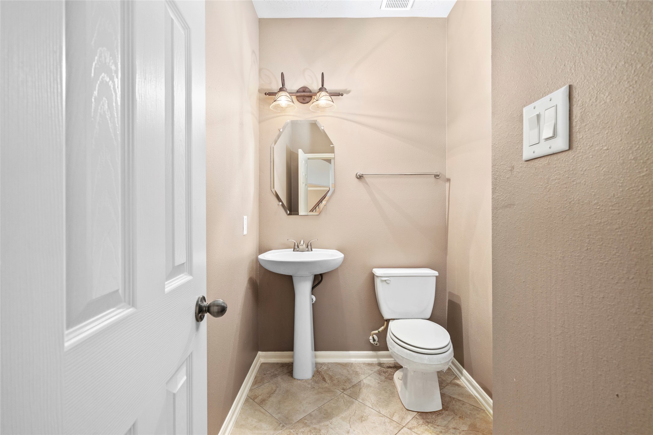 A chic powder bath welcomes guests with a graceful pedestal sink, designer octagonal mirror, and warm tile flooring, refined convenience on the main floor.