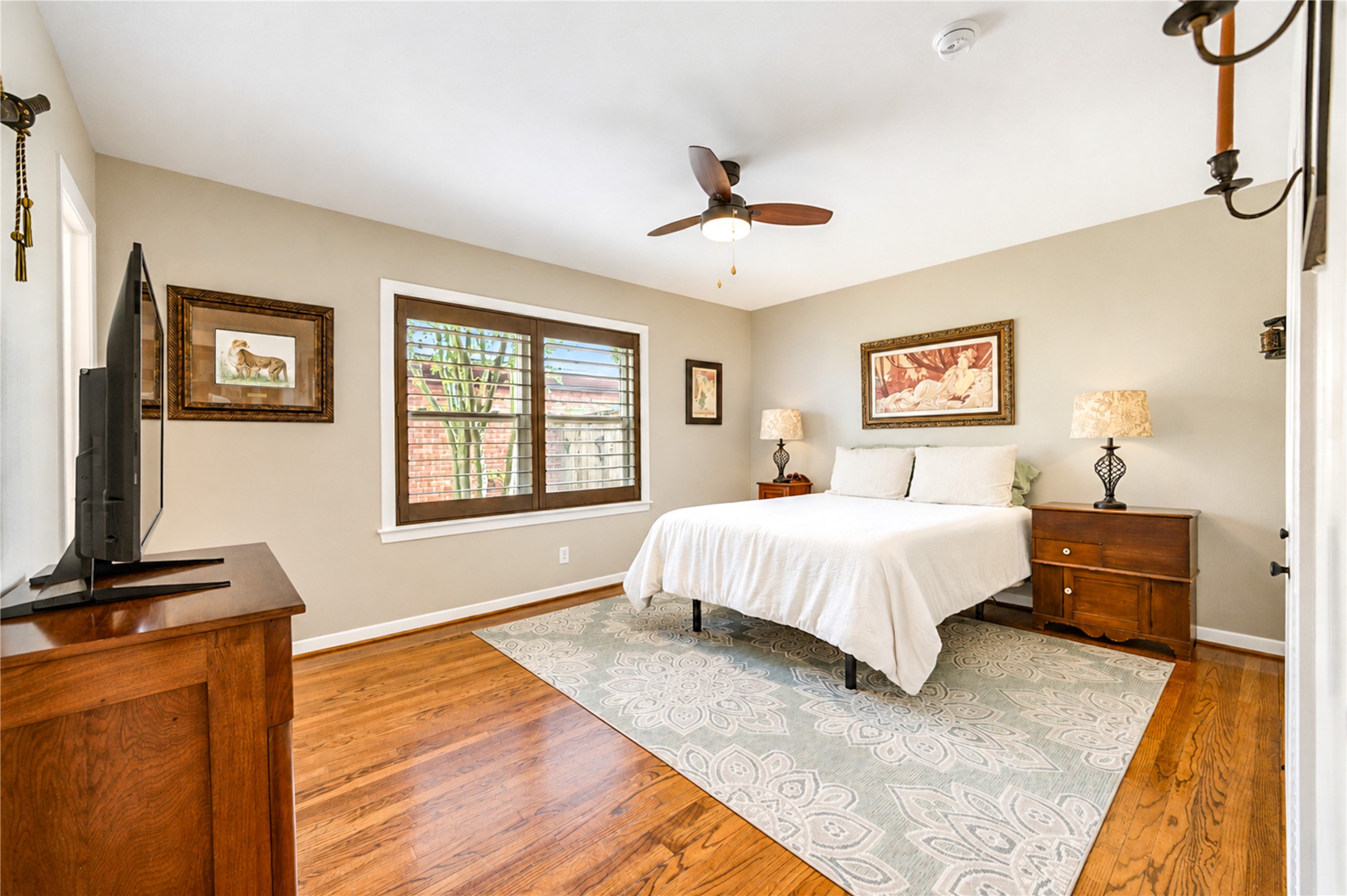 Plantation shutters and hardwood flooring continue in this bedroom, where large windows bring in natural light.