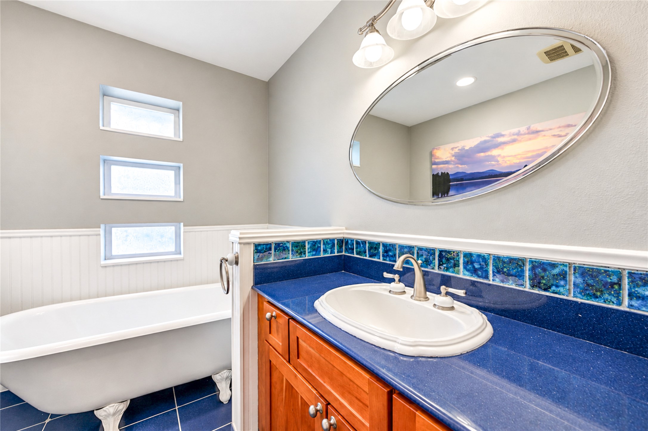 A classic clawfoot tub, rich blue countertop, decorative tile and a trio of accent windows give this charming bathroom distinctive character.