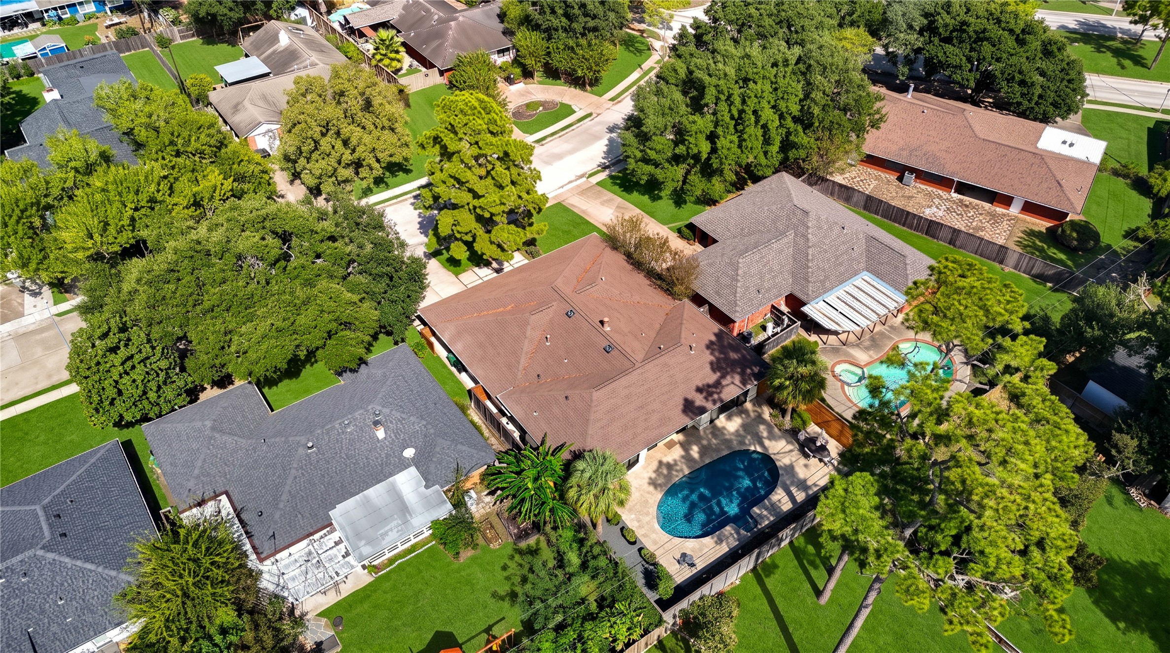 An aerial view of the rear of the home shows the pool, yard and surrounding mature tree canopy.