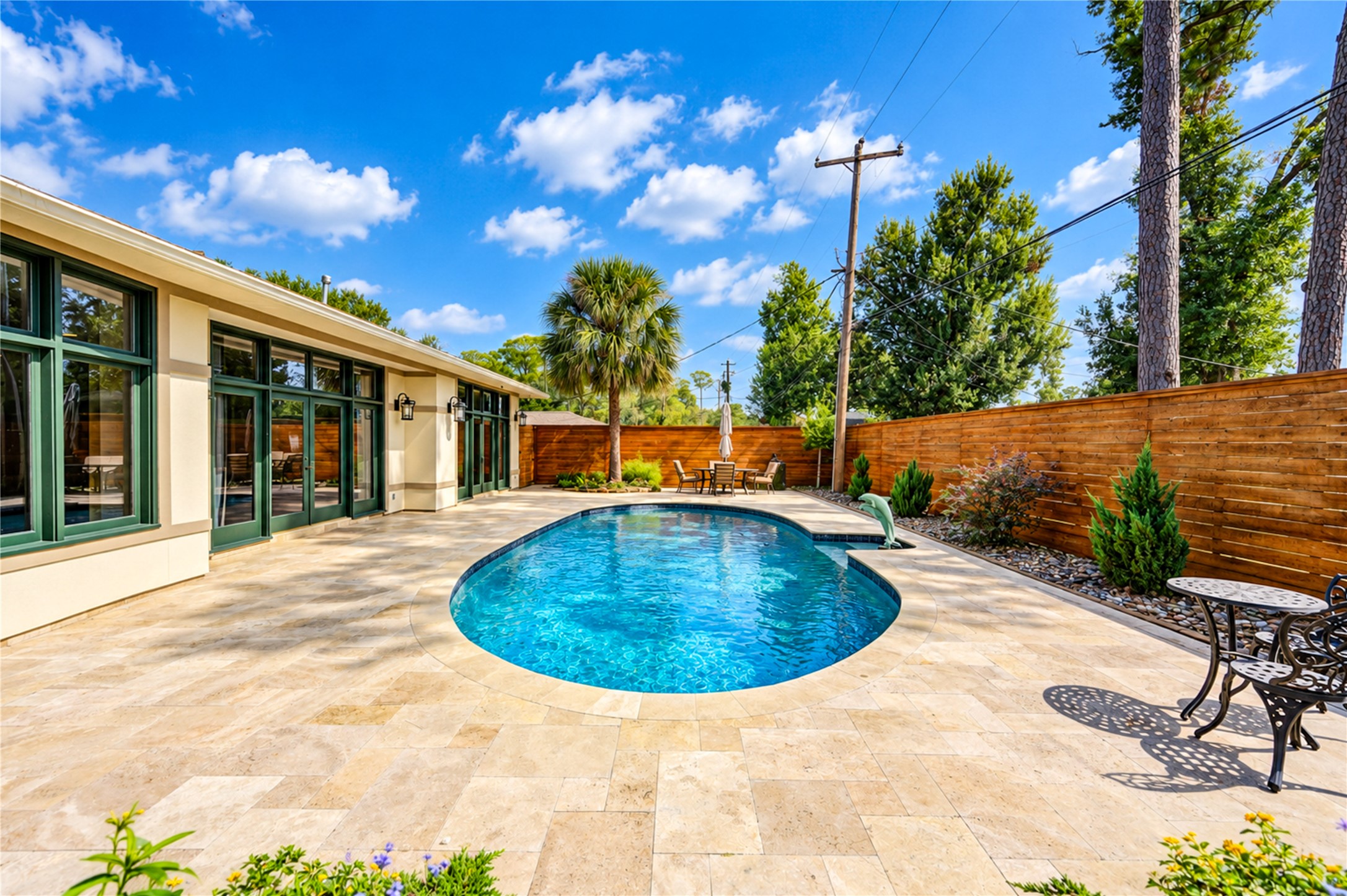 A travertine terrace curves around the pool along the rear of the home, with expansive wood-framed glass and French doors overlooking the water.