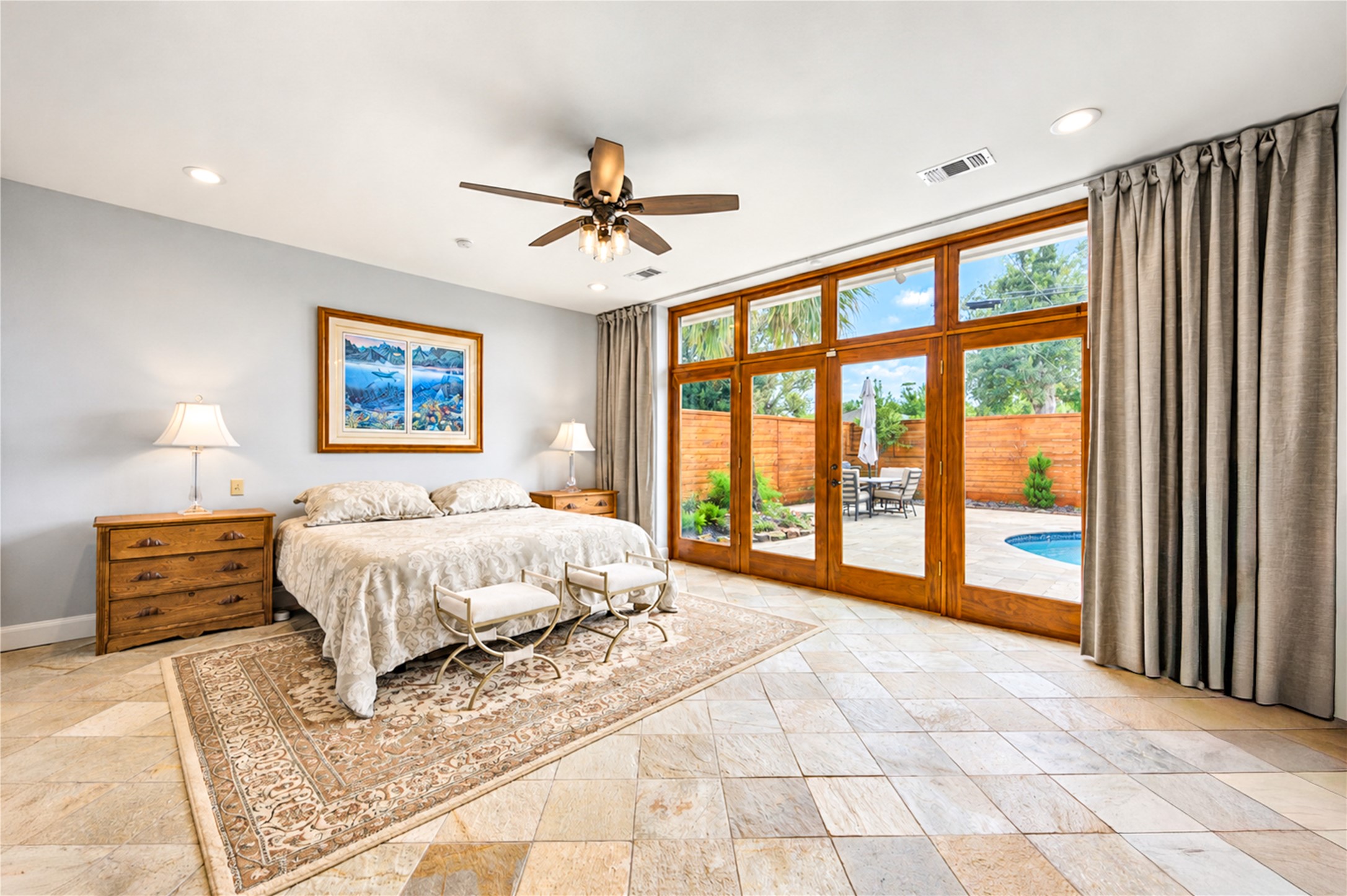 Glass doors and a wall of windows draw natural light into the primary suite and frame views of the pool.
