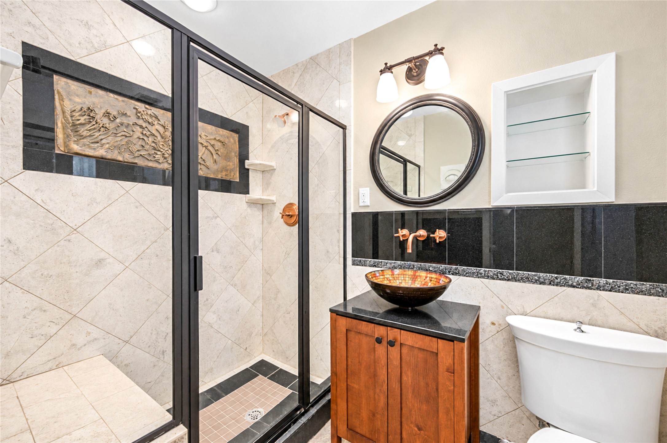 A framed glass shower with large-format tile, a granite accent band and a vessel sink on a wood vanity create a refined bath.