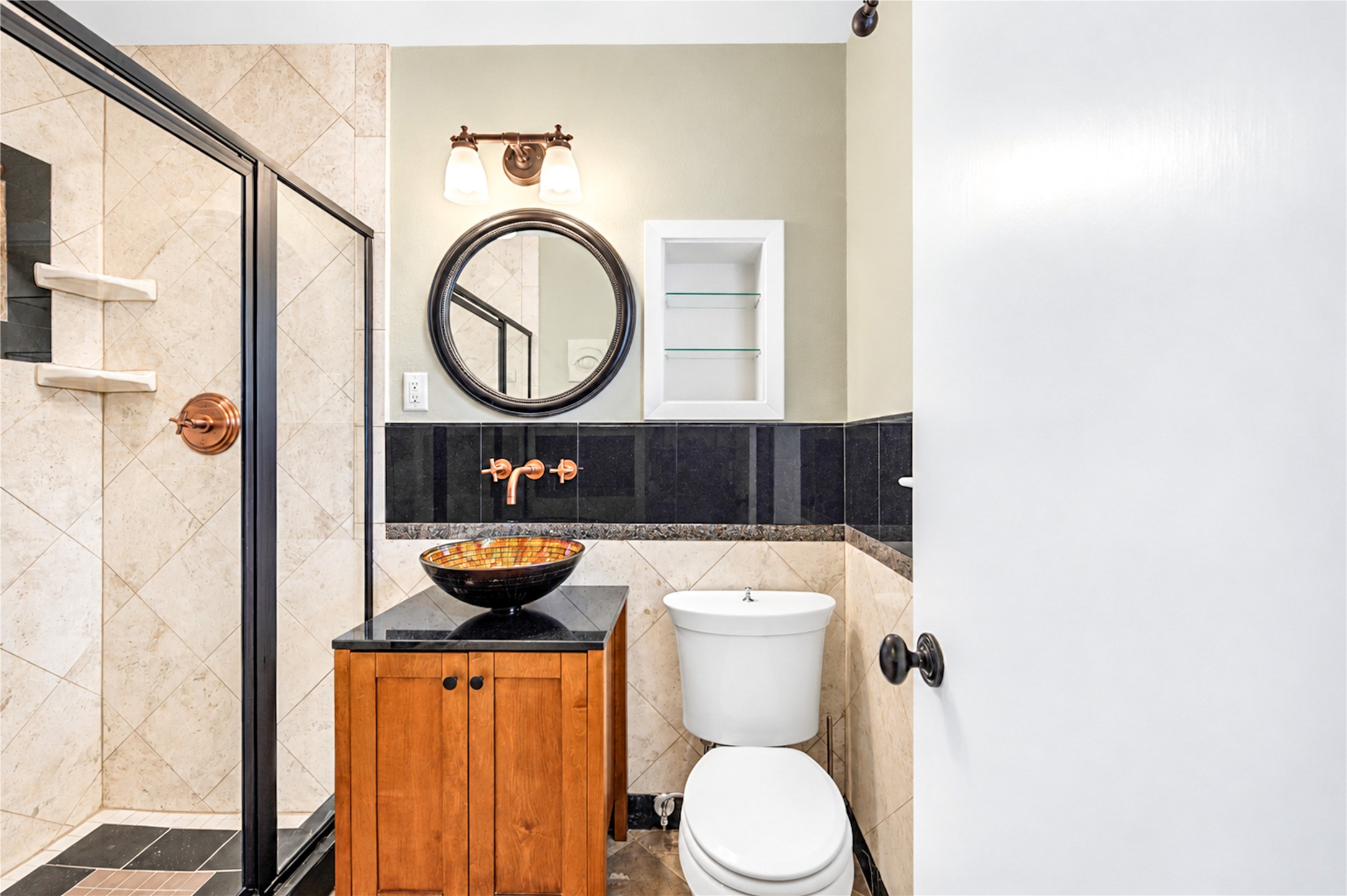 A vessel sink, black granite backsplash, round mirror and recessed shelving give this bath a distinctive, finished character.