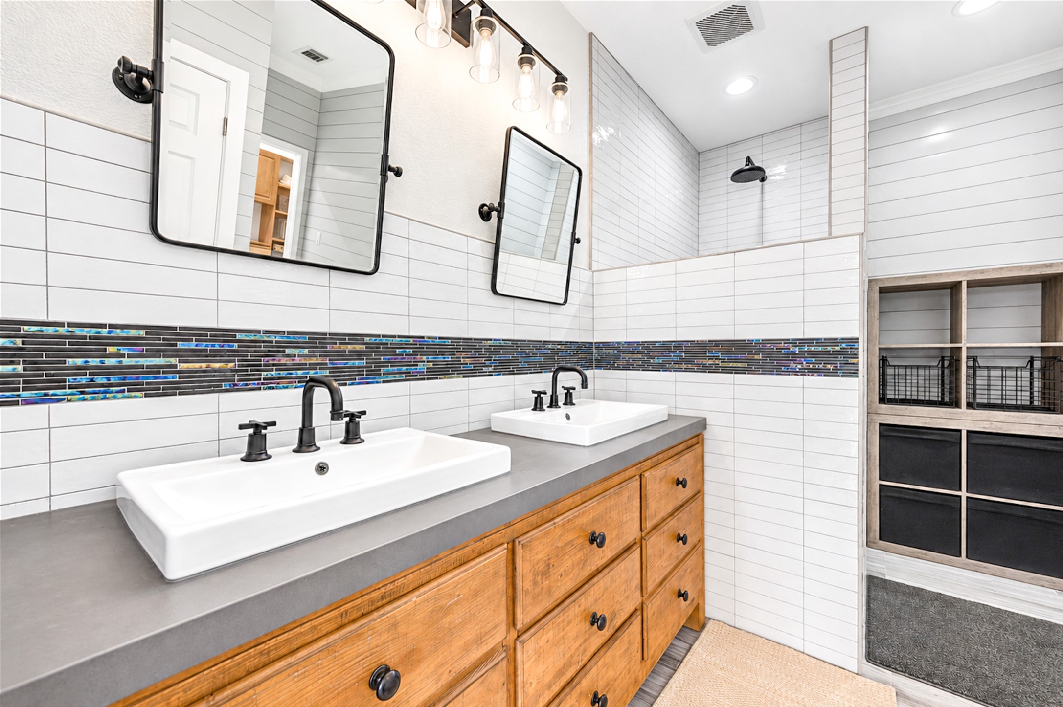 A dual vessel-sink vanity and framed mirrors anchor the primary bath, with the walk-in shower and built-in storage beyond.
