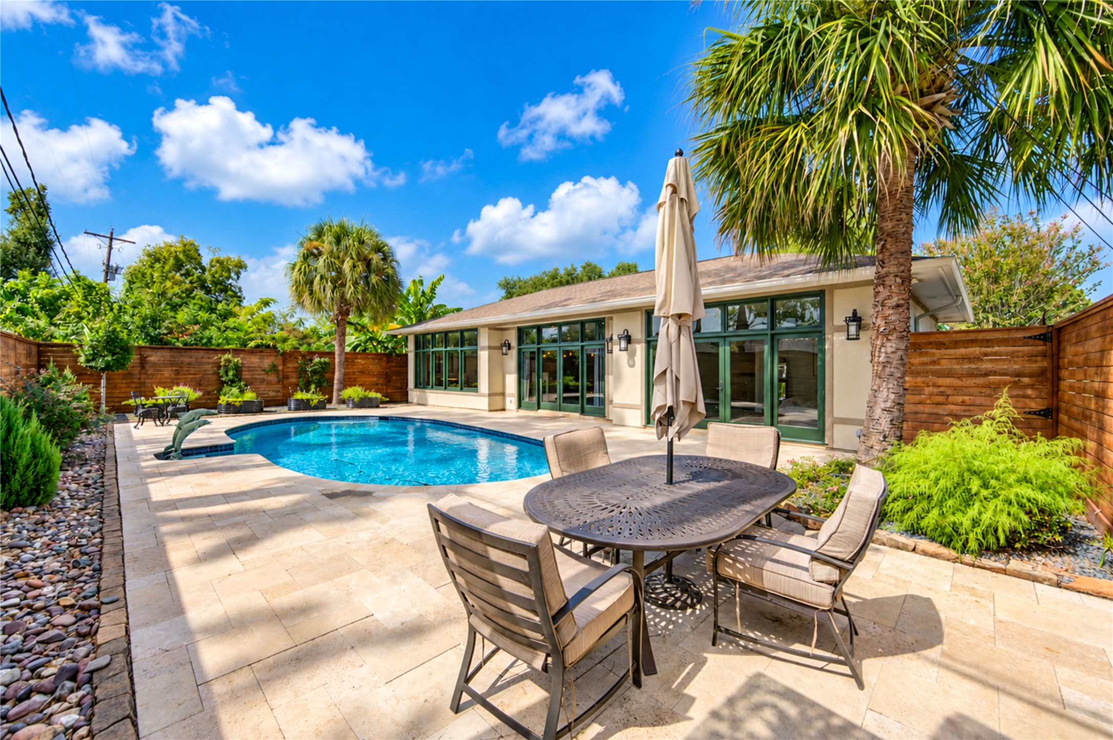 A travertine terrace with room for outdoor dining wraps the pool, with palms and wood fencing for privacy.