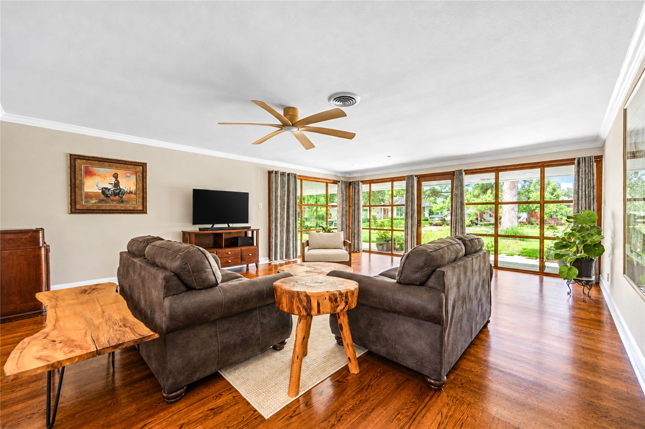 A wall of wood-framed windows frames garden views and fills the living room with natural light above rich hardwood flooring. A wall of wood-framed windows frames garden views and fills the living room with natural light above rich hardwood flooring.
