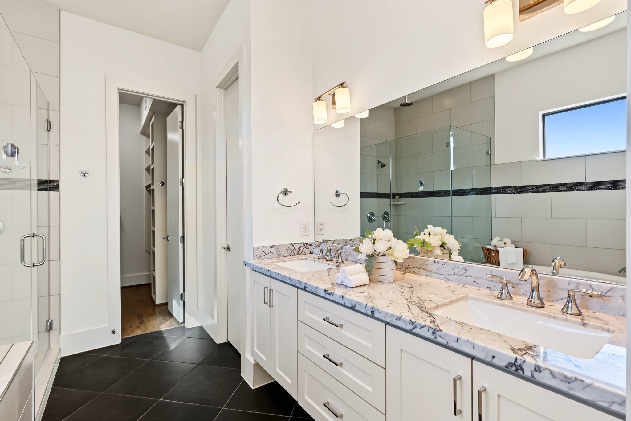 Choose between an invigorating rinse or a leisurely soak in the six-foot oval tub. A sleek, frameless glass shower enclosure featuring dual fixturesboth a wall-mounted head and an overhead rain showerelevates the daily routine into a spa-like ritual.