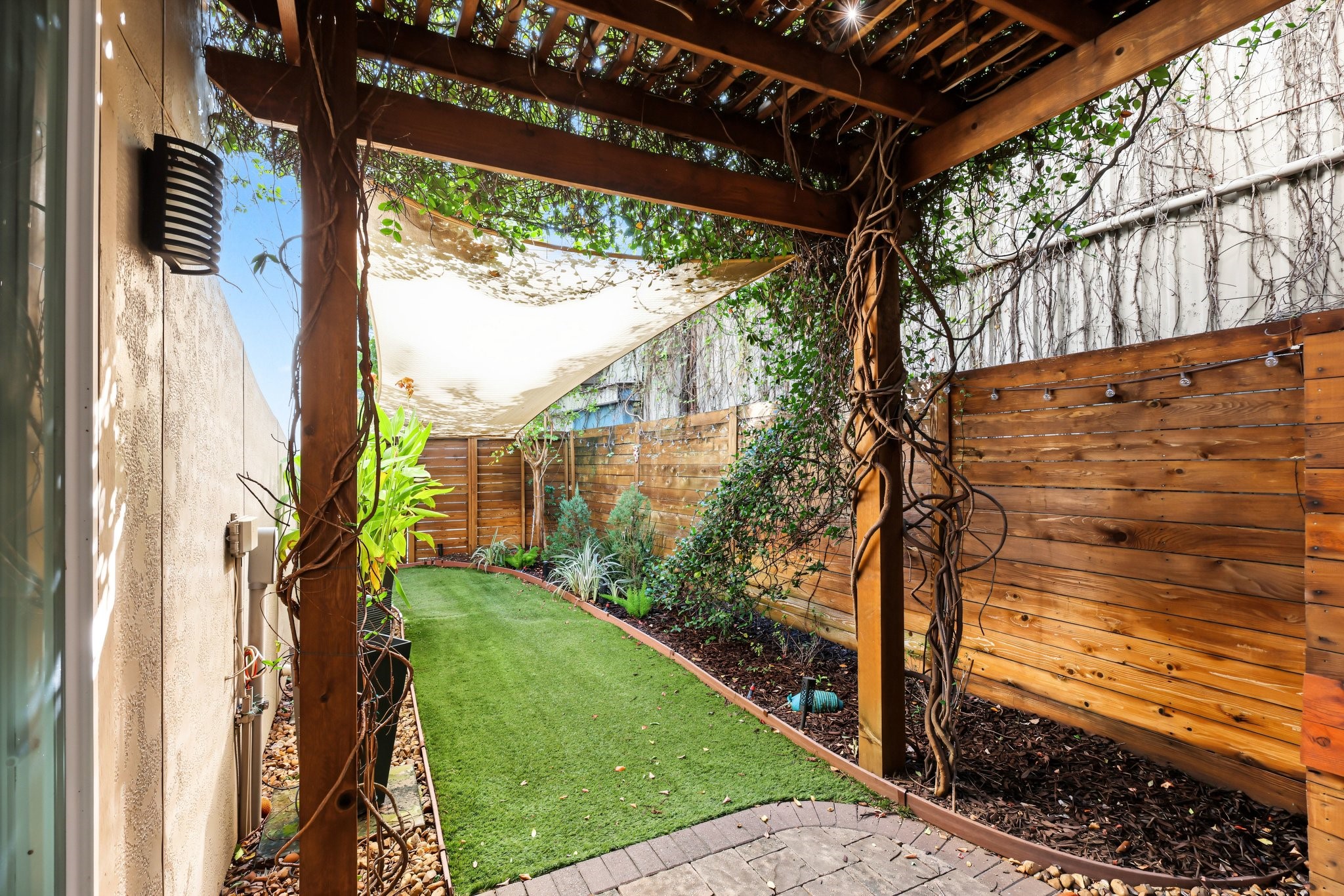 Step outside to a private, low-maintenance backyard where pristine artificial turf meets gracefully curved garden beds. Ornamental greenery and climbing ivy soften the fencing, creating an inviting, verdant open-air retreat without the upkeep of a traditional lawn.