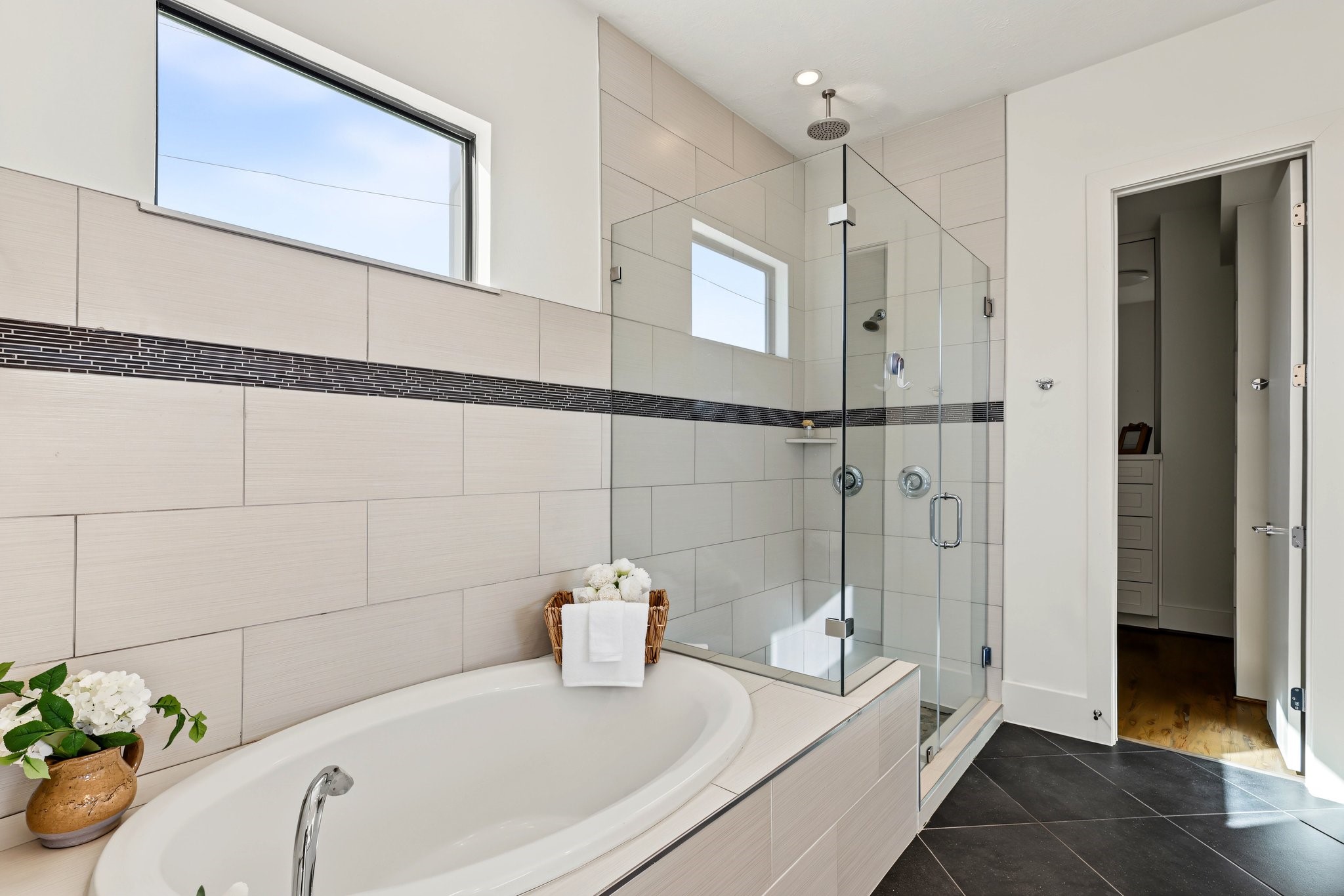 Refresh beneath an overhead rainfall showerhead or sink into the six-foot oval soaking tub. A sleek frameless glass enclosure, expansive large-format tile, and delicate mosaic accents infuse the primary bath with a serene, spa-inspired aesthetic, while a high-set window ushers in abundant natural light and privacy.