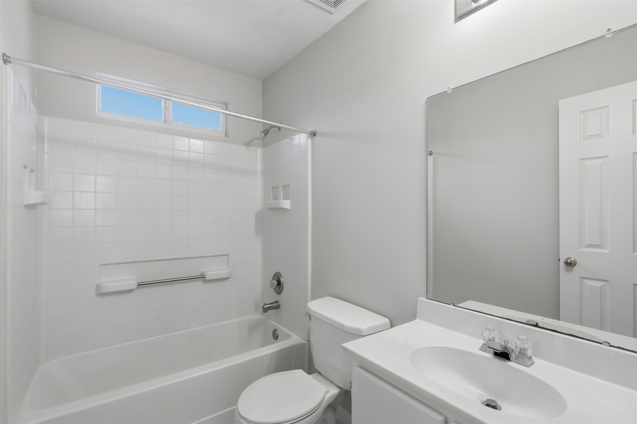 Bright upper-level secondary bath equipped with elegant marble-look tile flooring, a tub/shower combination, white vanity, and a high transom window that lets in natural light while maintaining privacy.