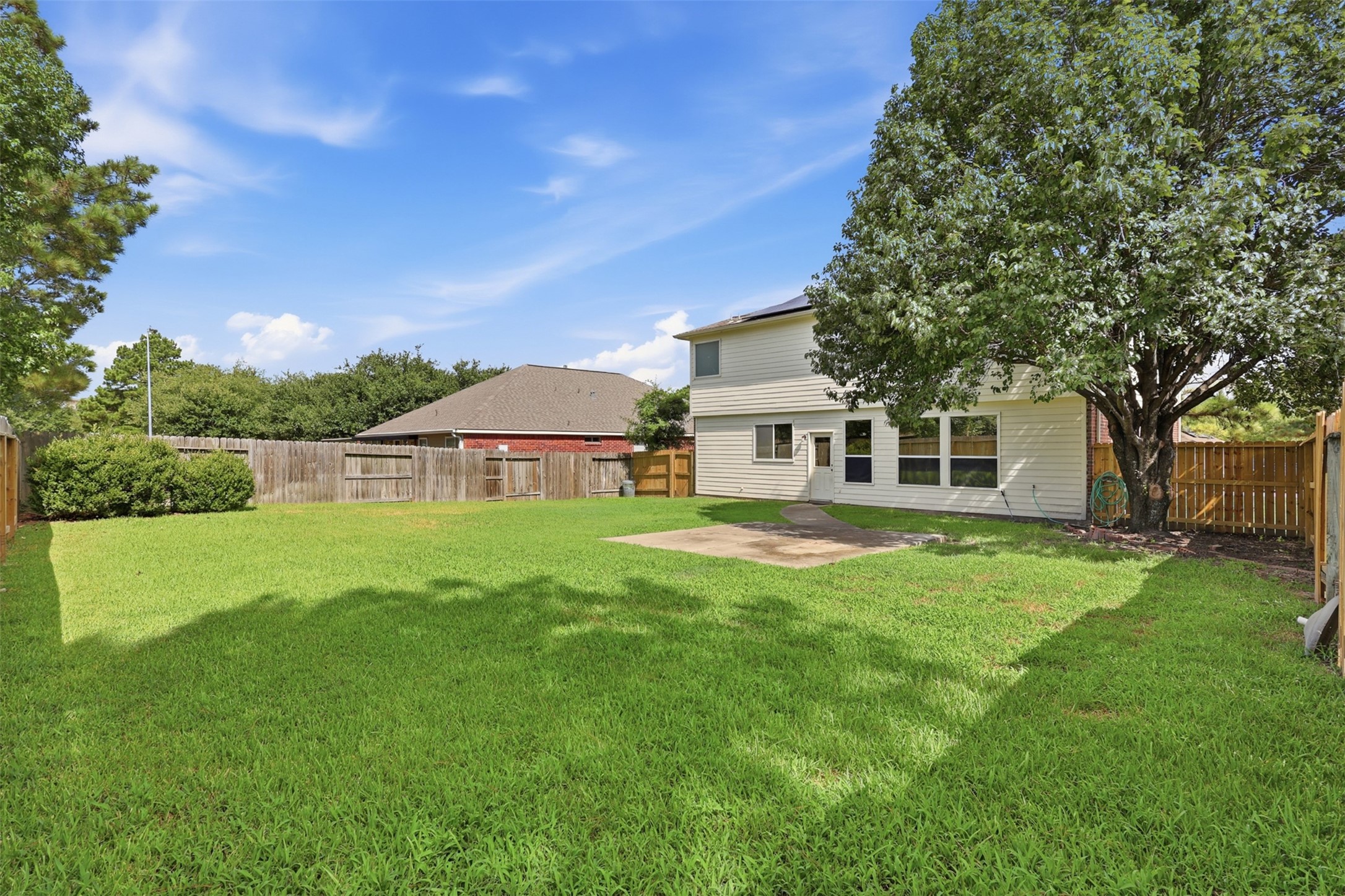 Rear view showcasing the generous lot size, concrete patio slab, beautiful shade tree, and direct walkway access to the homeoffering plenty of room for pets, kids, or a future pool.