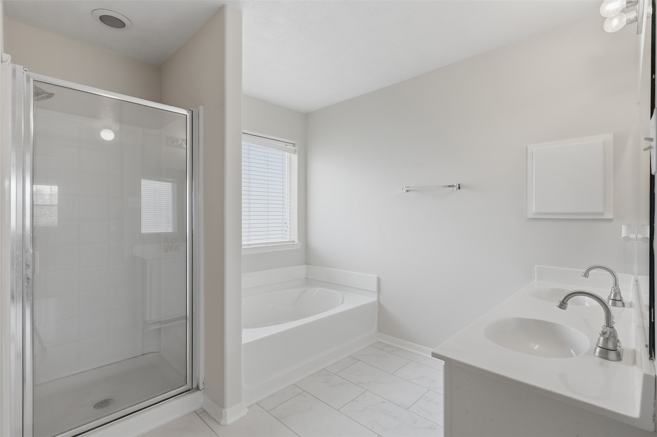 Continuing from the private entry landing, the primary en-suite opens into a bright, spacious bath featuring a double vanity, walk-in glass shower, deep soaking tub, and marble like tile flooring.