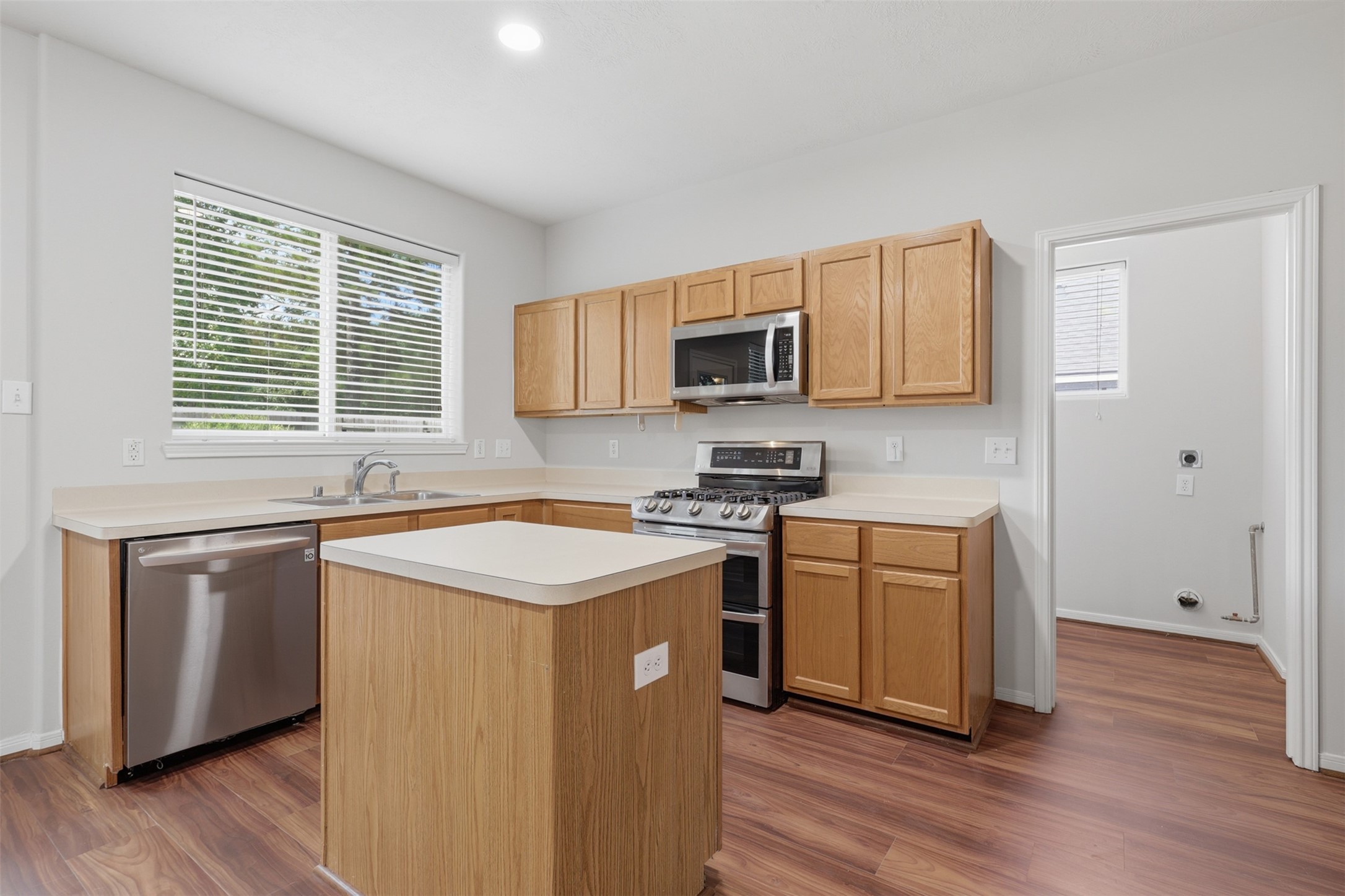 Spacious, well-appointed kitchen featuring abundant oak cabinetry, ample counter space, stainless steel appliances, a center island, double-basin sink, and warm wood-look flooring.