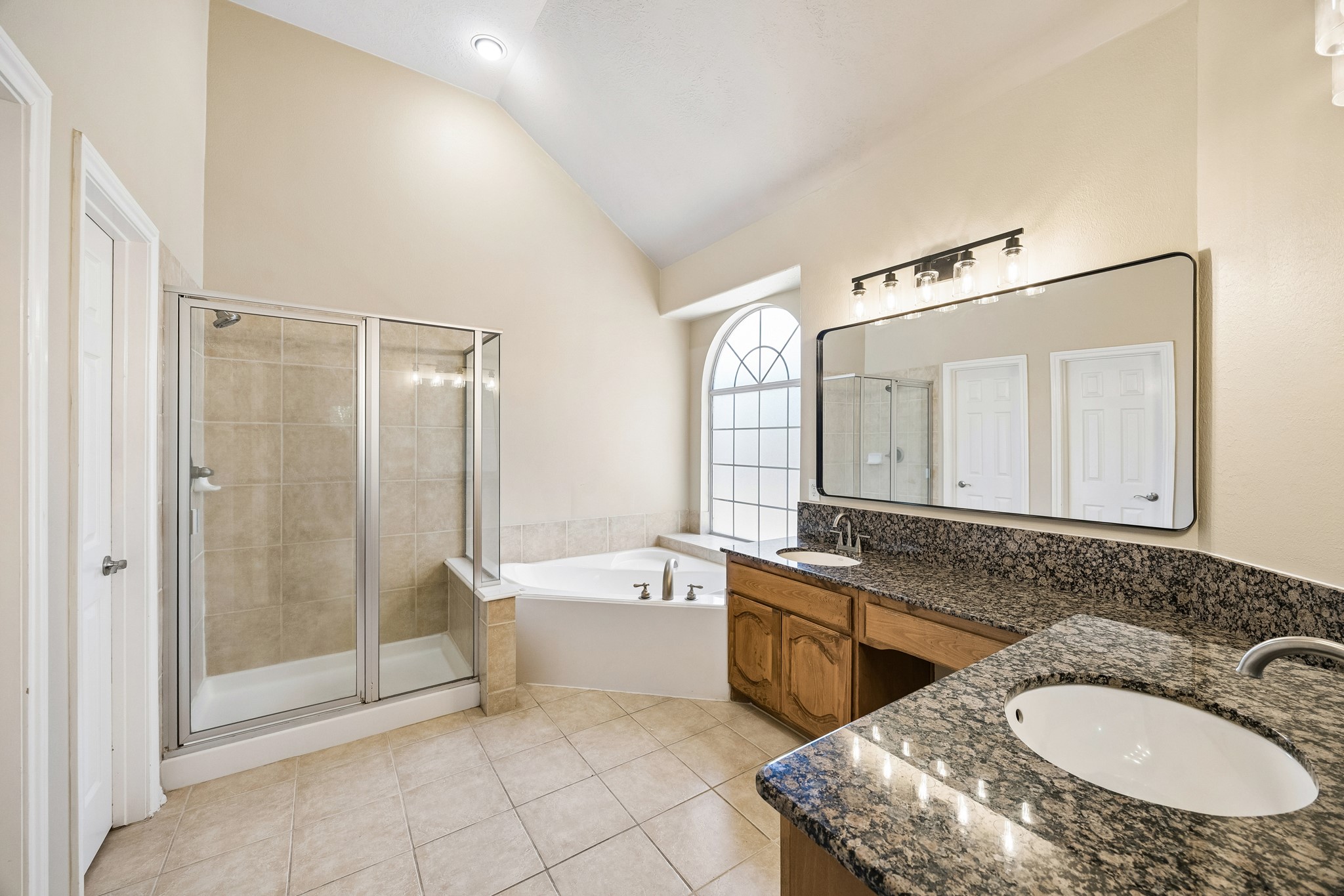 Spacious primary bath features dual vanities with generous counter space, a large soaking tub, separate glass-enclosed shower, abundant cabinetry, and natural light, creating a comfortable and functional private retreat.