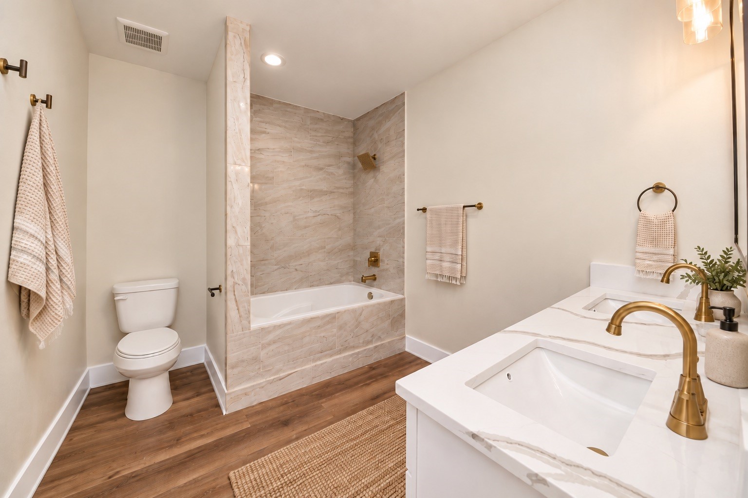 Private primary bathroom featuring a soaking tub with decorative tile surround, quartz vanity countertop, modern cabinetry, updated fixtures & attractive gold-tone hardware.