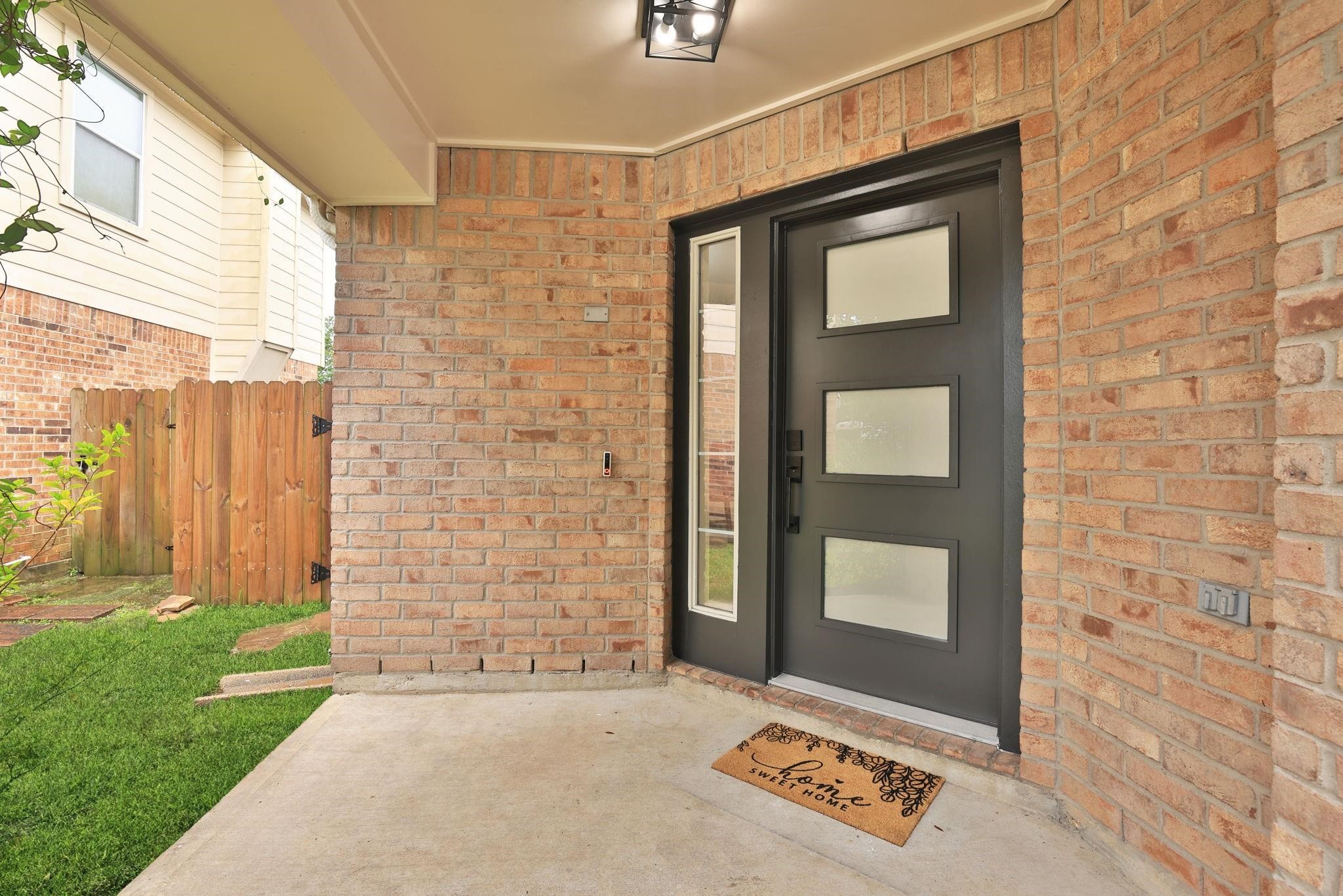 A close-up look at the modern frosted glass panel front door and a ring doorbell. Exterior also has new light fixtures.
