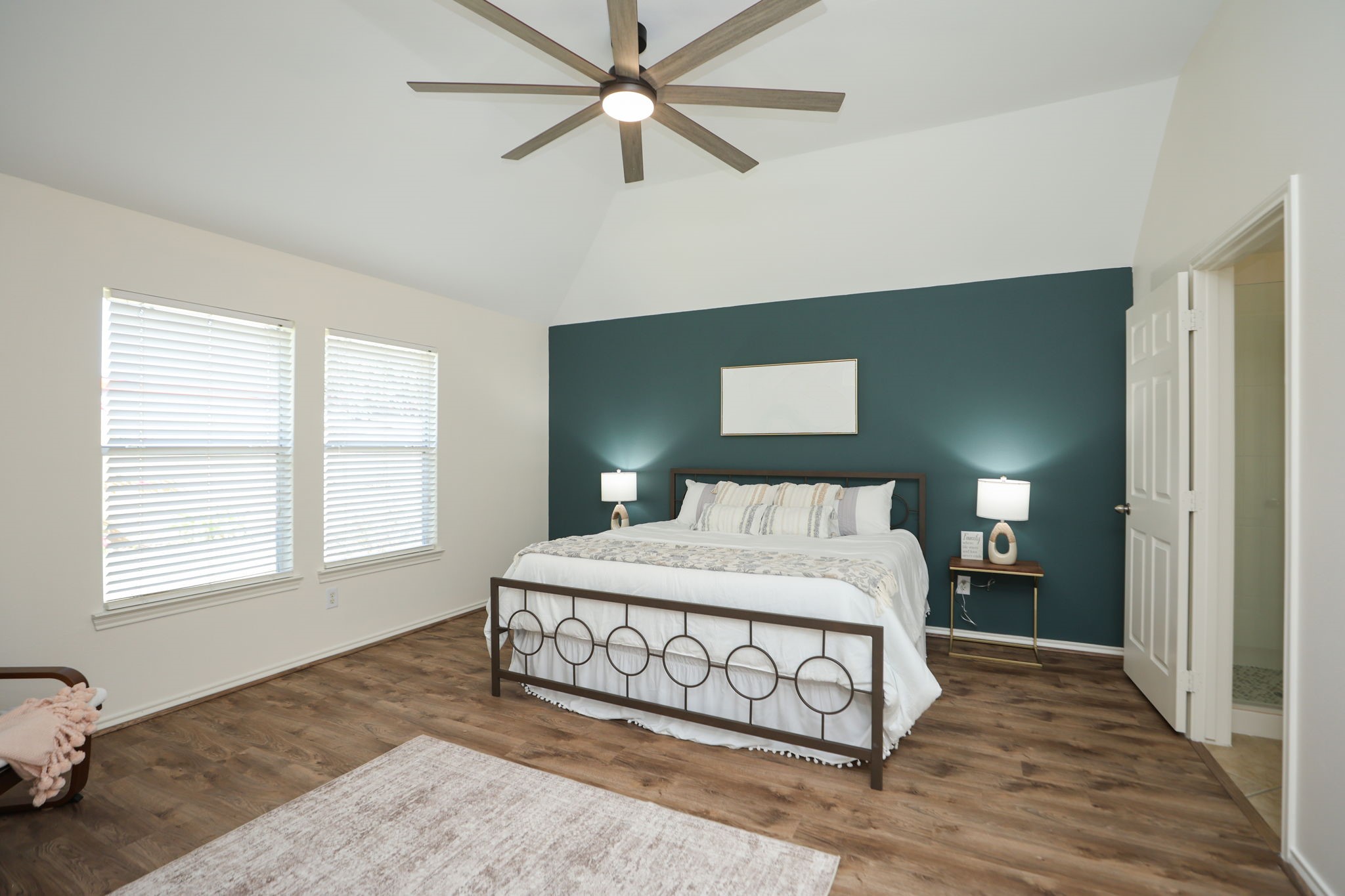 Peaceful primary suite in the rear of the home, also featuring an 8 blade fan, Hidden Gem accent wall, and modern LVP flooring. Primary bath is to the right of this photo.