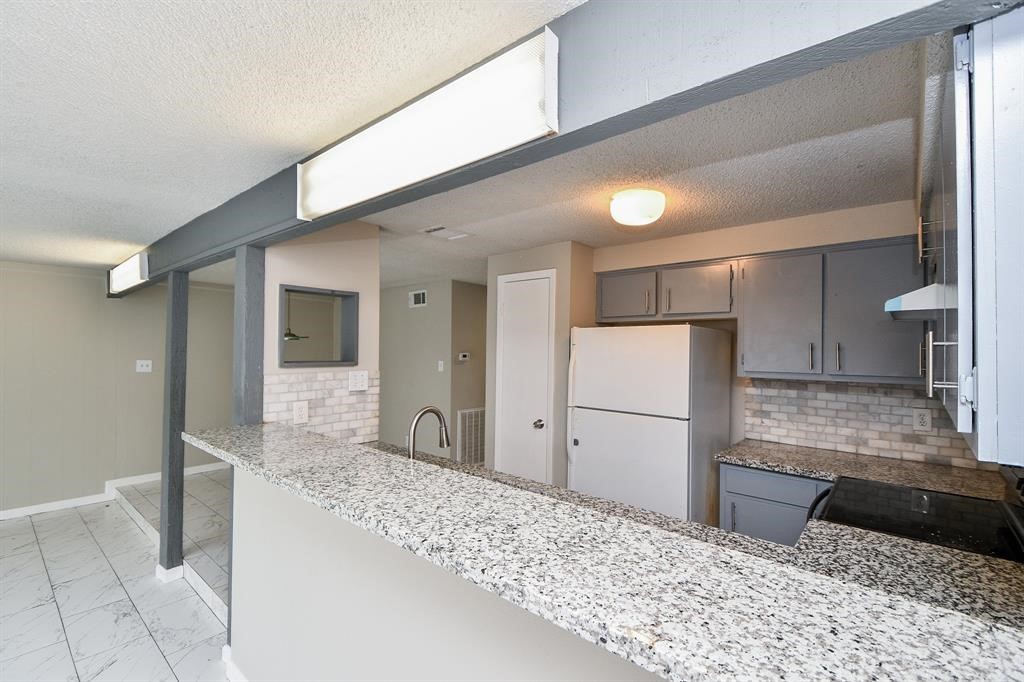 Modern kitchen with granite countertops, ample cabinet space, and a breakfast bar. Neutral tones and tile flooring create a bright, open atmosphere.