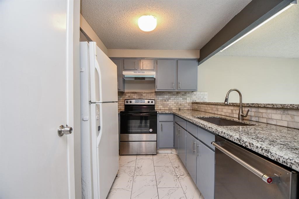 Modern kitchen with sleek granite countertops, stainless steel appliances, and light gray cabinetry. The space features a tiled backsplash and a clean, bright atmosphere.