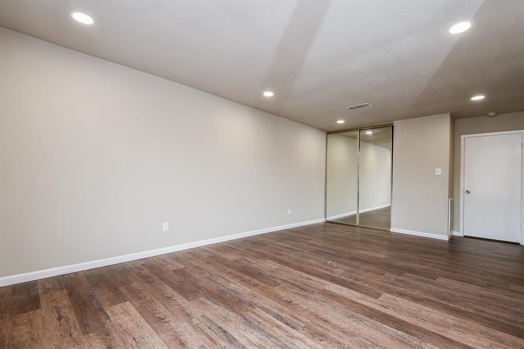 This room features a spacious layout with wood-style flooring, recessed lighting, and neutral walls. It includes a mirrored sliding closet door and a white door, offering a modern and clean look.