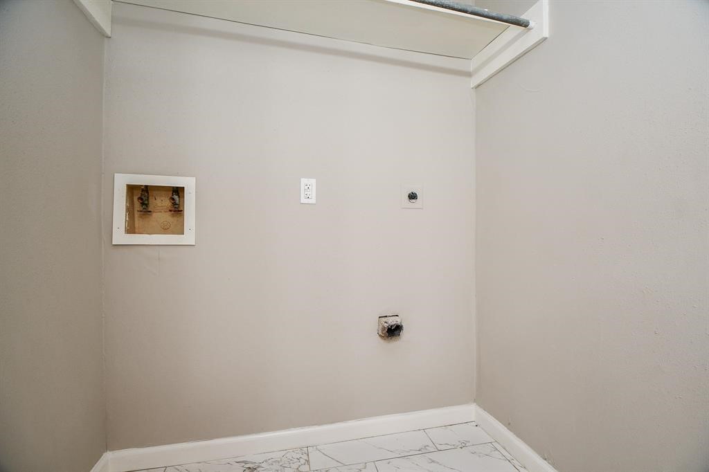 This photo shows a laundry area with hookups for a washer and dryer. It features light-colored walls and tiled flooring, providing a clean and functional space for laundry appliances.