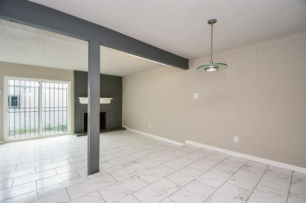 This room features a spacious open layout with light tile flooring and neutral walls. It includes a cozy brick fireplace, sliding glass doors leading outside, and a modern ceiling light fixture. Ideal for a living or dining area.