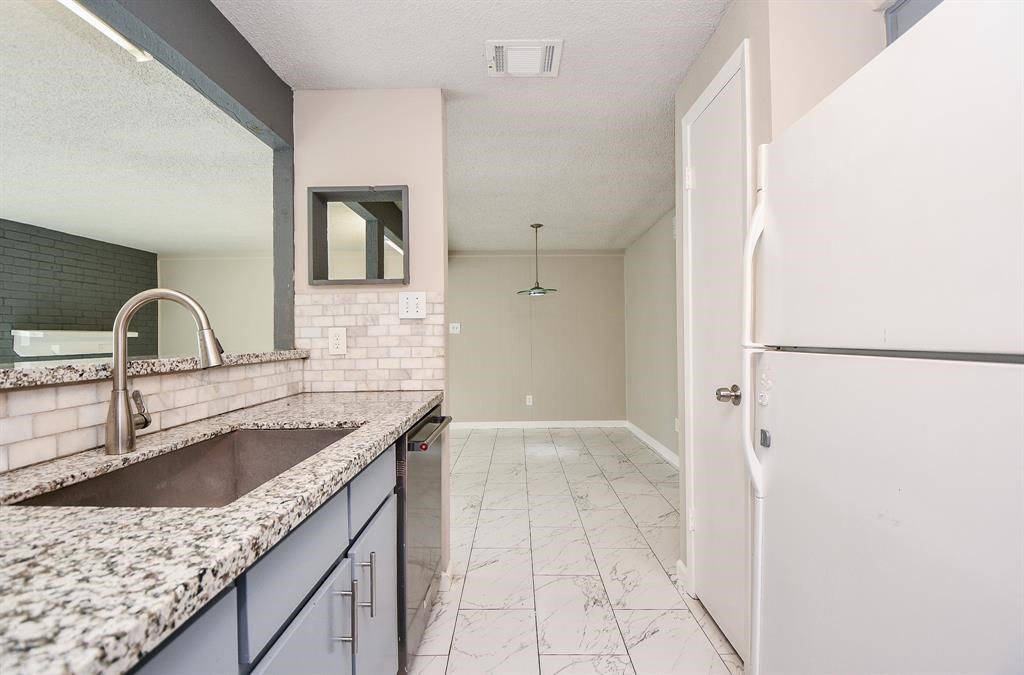 This photo showcases a modern kitchen with granite countertops, a large sink, and sleek cabinetry. It opens into a dining area with tiled flooring and neutral walls, offering a bright and open feel.