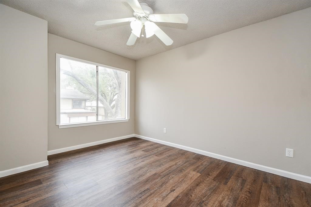 Bright, airy room with a large window, ceiling fan, and wood flooring, perfect for a cozy bedroom or office space.